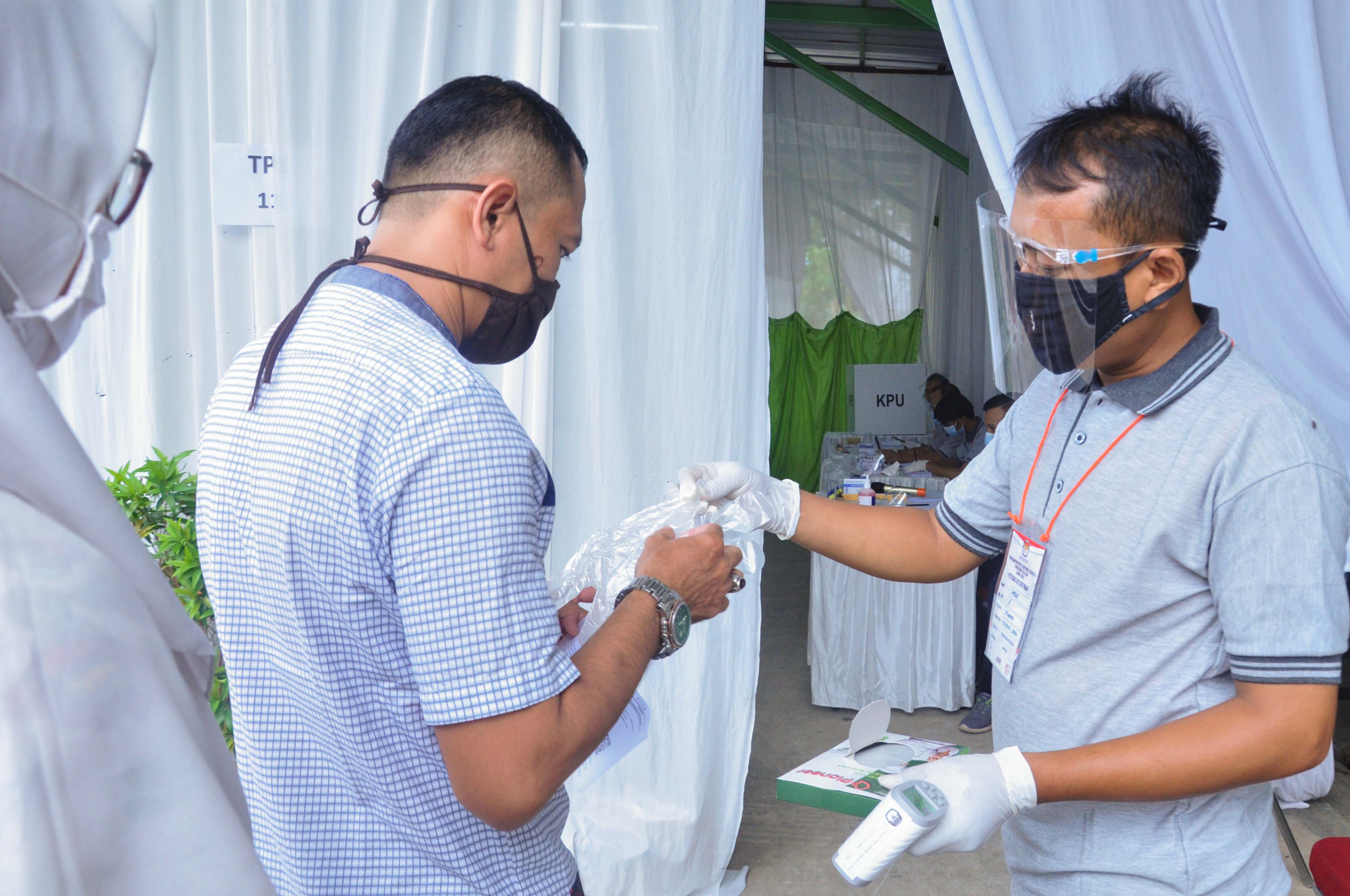 Petugas KPPS memberikan sarung tangan plastik kepada warga yang datang ke TPS 12, Graha Mas Serpong