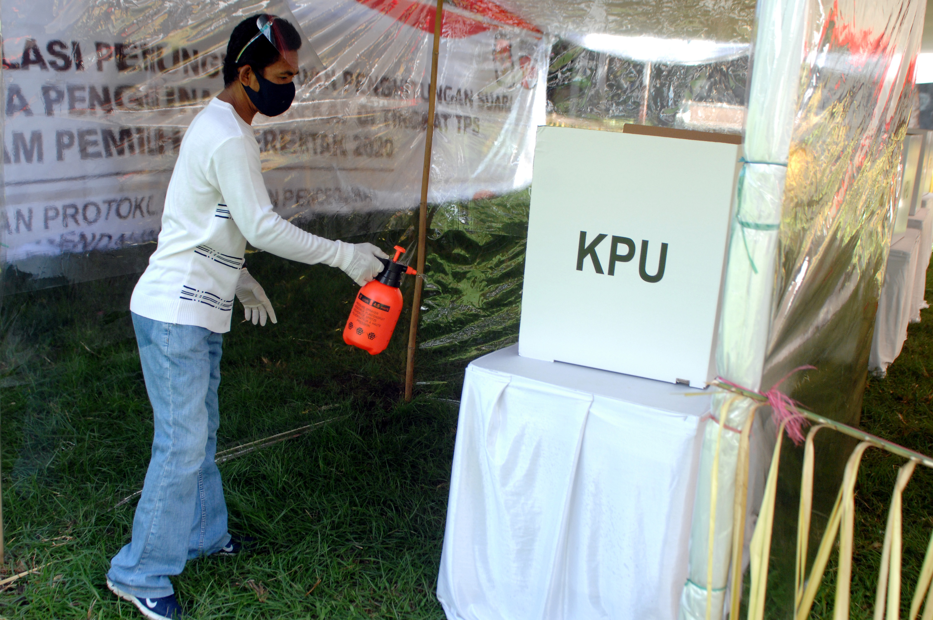 Petugas KPPS menyemprotkan cairan disinfektan ke bilik khusus pemungutan suara di Manado, Sulawesi Utara.