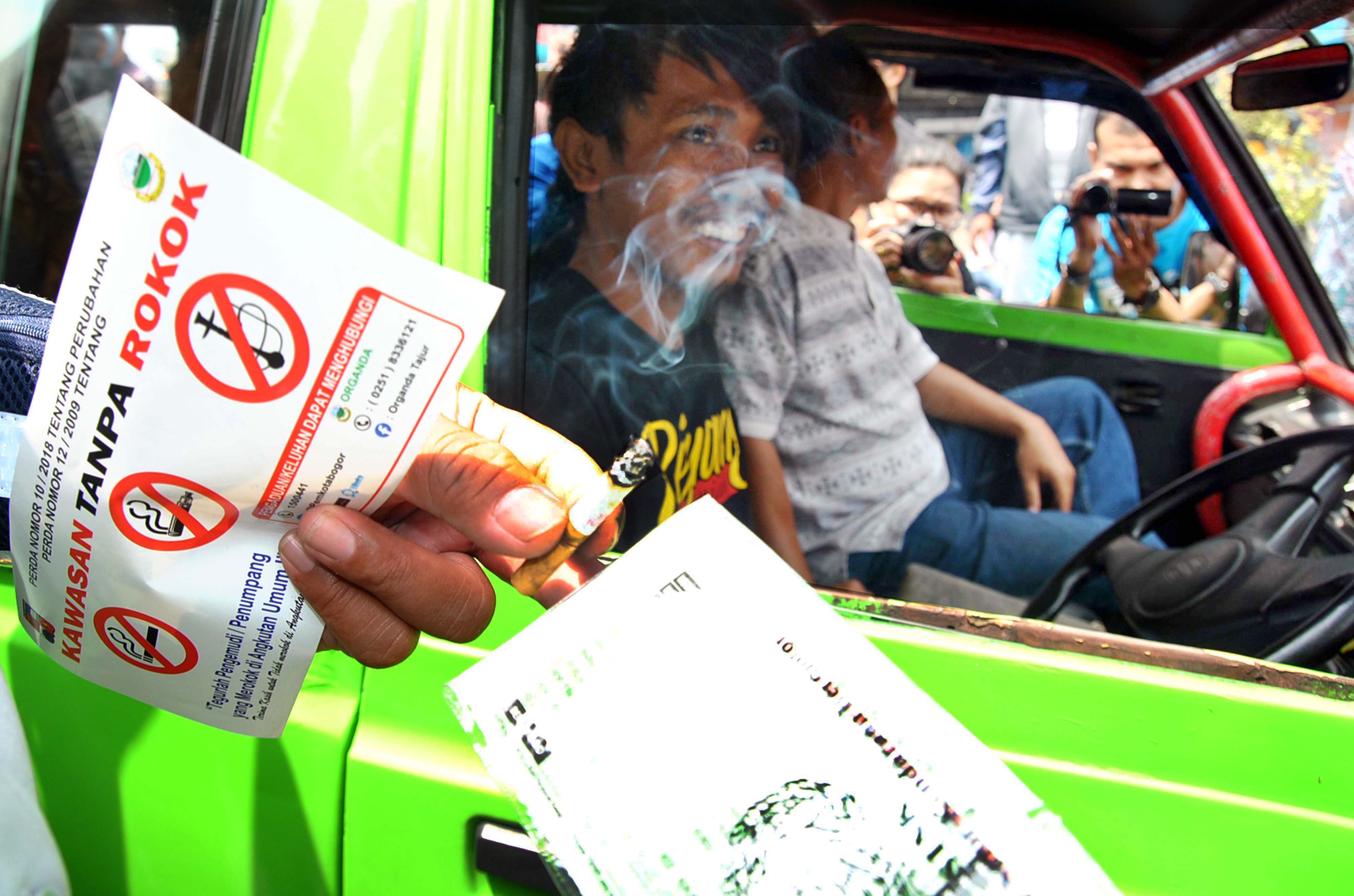 Petugas Satpol PP Kota Bogor mengambil rokok yang dihisap sopir angkot. Merokok menjadi pemicu terjadinya kanker paru. 