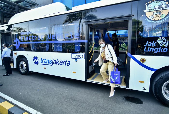 Penumpang TransJakarta yang mengenakan masker turun dari kendaraan. 