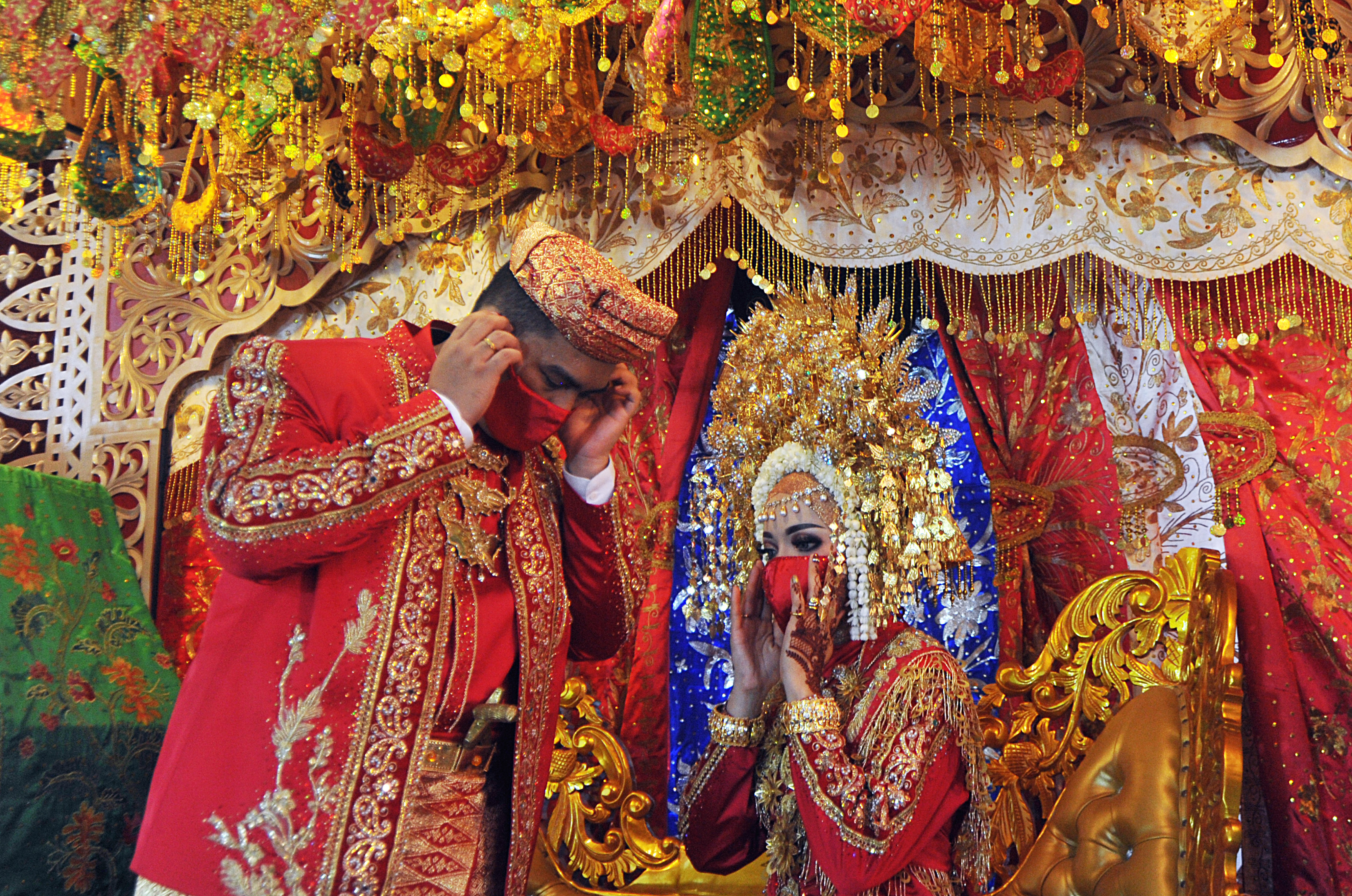 Pasangan pengantin merapikan masker saat resepsi pernikahan Minang atau Baralek, di Lubukbuaya, Padang, Sumatra Barat.