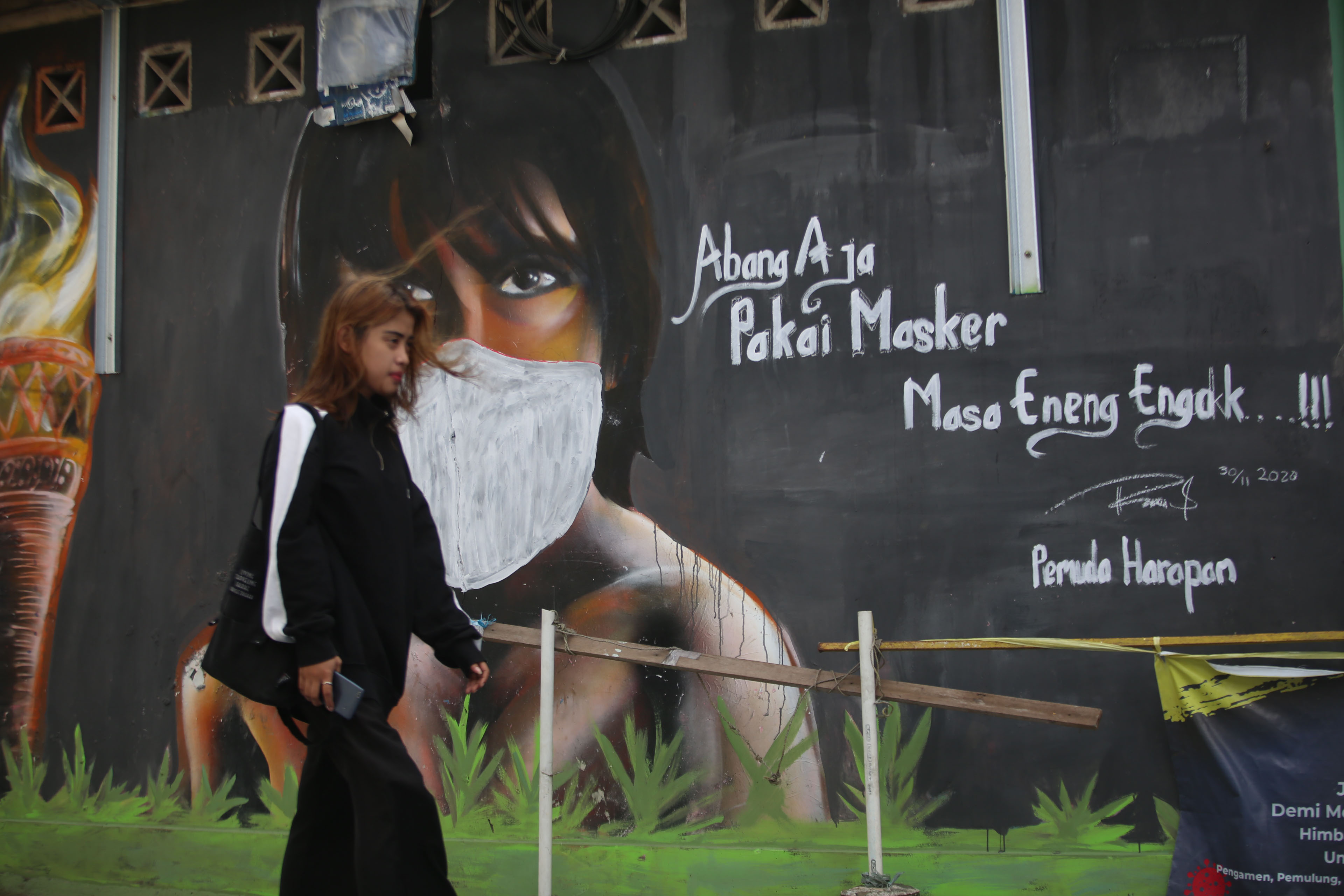 PERKEMBANGAN KASUS COVID-19 DI JAKARTA: Warga melintas di depan mural berisi imbauan disiplin protokol kesehatan di Jakarta, Senin (14/12/20