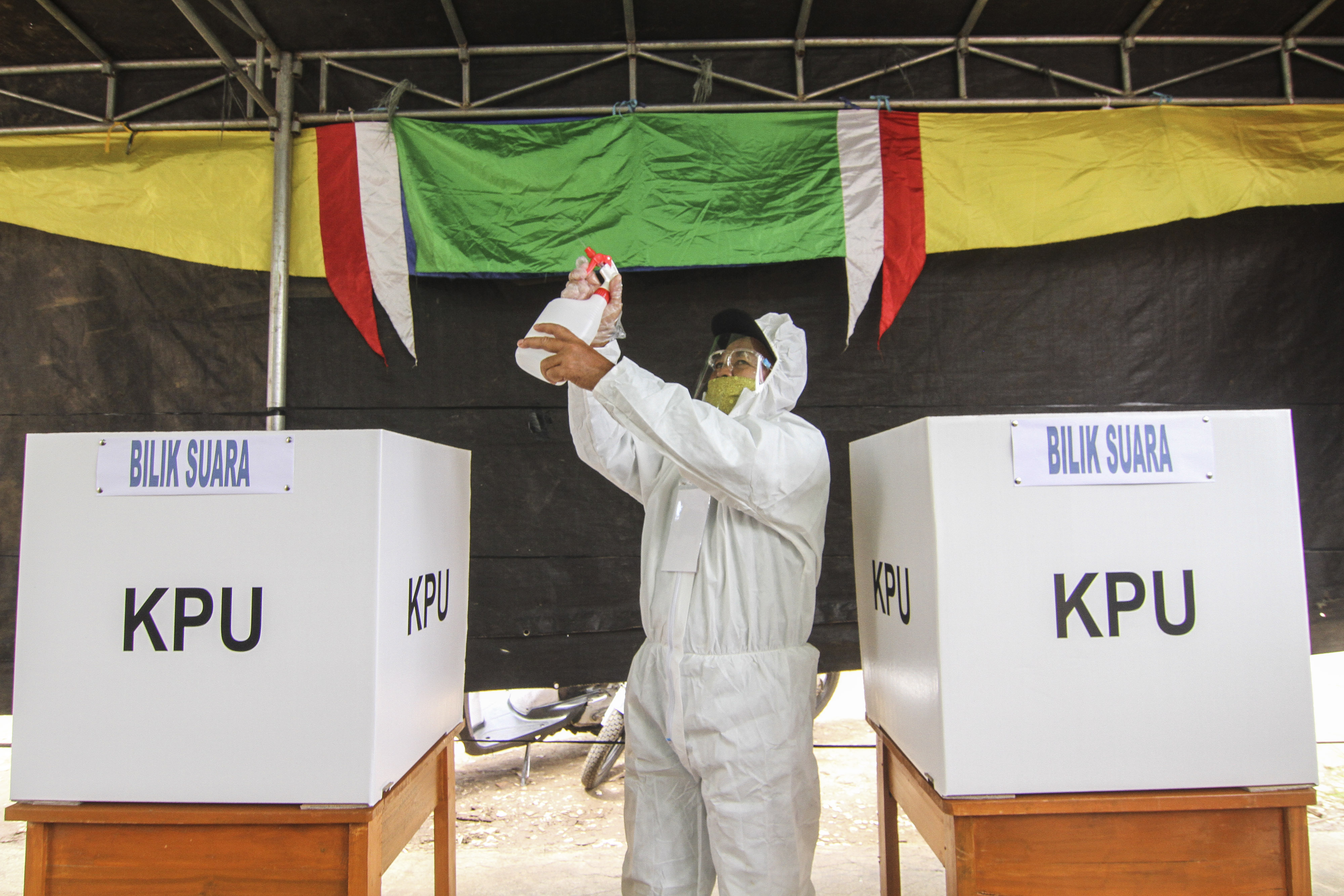 Petugas KPPS memakai alat pelindung diri menyemprotkan cairan disinfektan di TPS 13, Cipayung, Depok, Jawa Barat, Rabu (9/12).