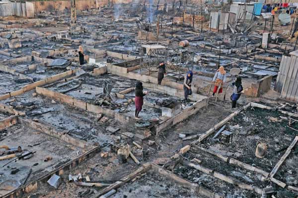 Pengungsi Suriah berada di antara reruntuhan tempat penampungan mereka yang terbakar