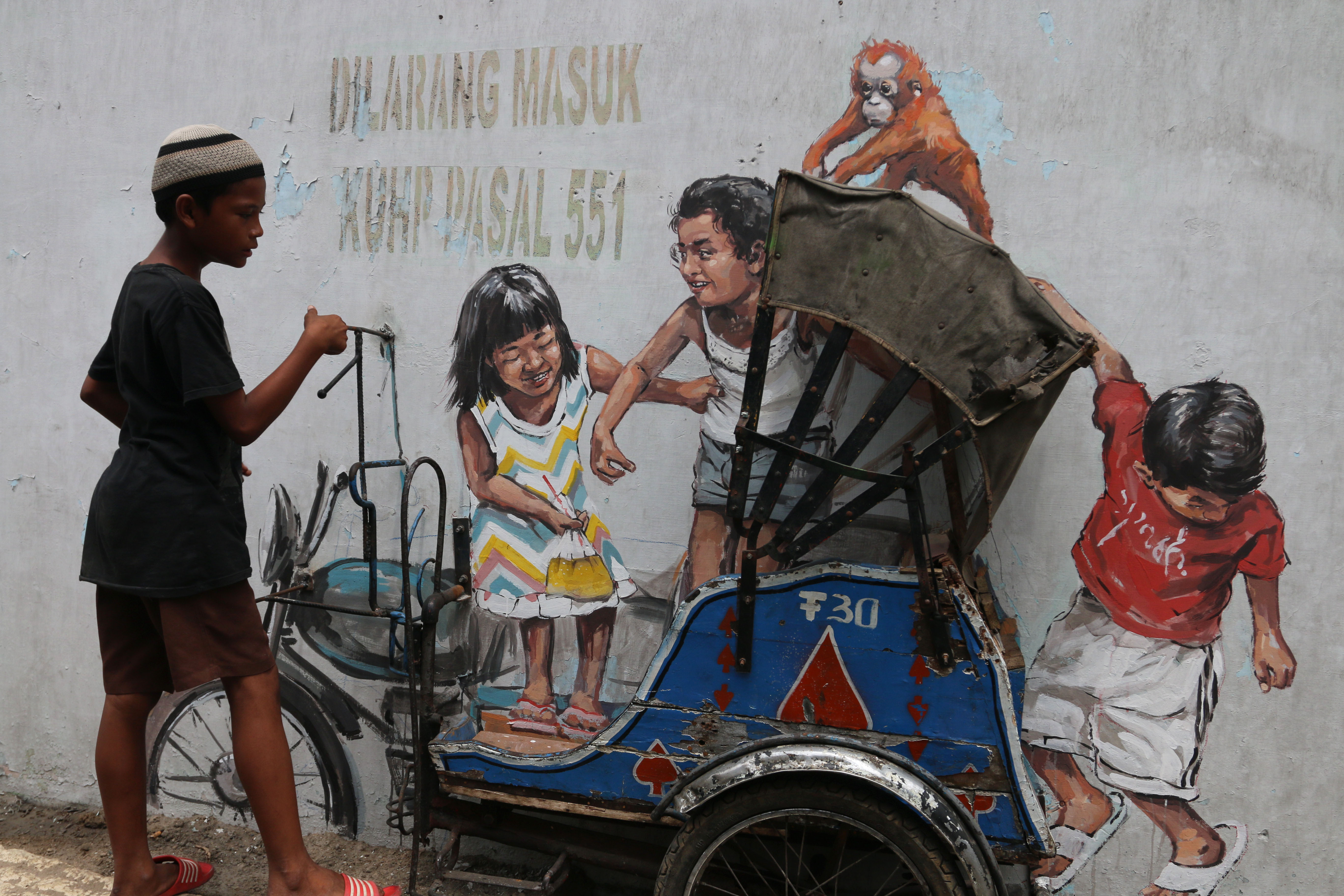 Seorang anak melihat mural yang digabungkan dengan miniatur becak di Jalan Perdana, Medan, Sumatrra Utara.