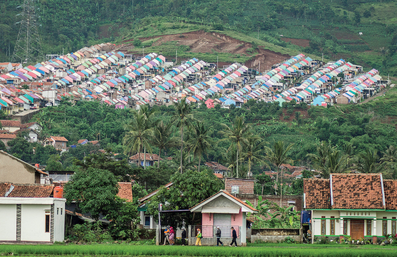 Warga berjalan dengan latar belakang deretan rumah di kawasan lereng perbukitan di Kabupaten Sumedang, Jawa Barat, kemarin.