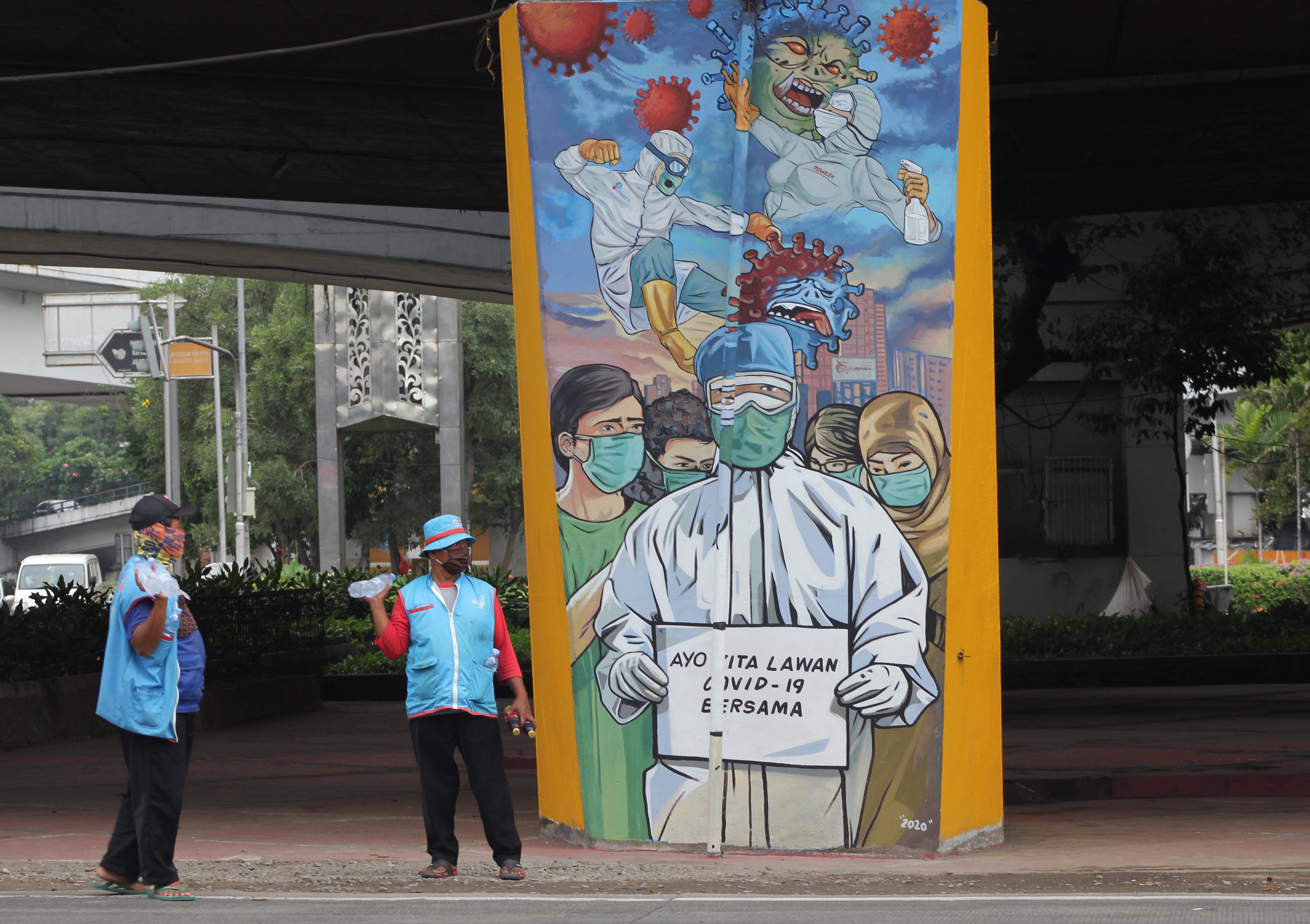 Pedagang angsongan menawarkan dagangan di depan Mural sosialisasi pencegahan penularan covid-19 di Jakarta.