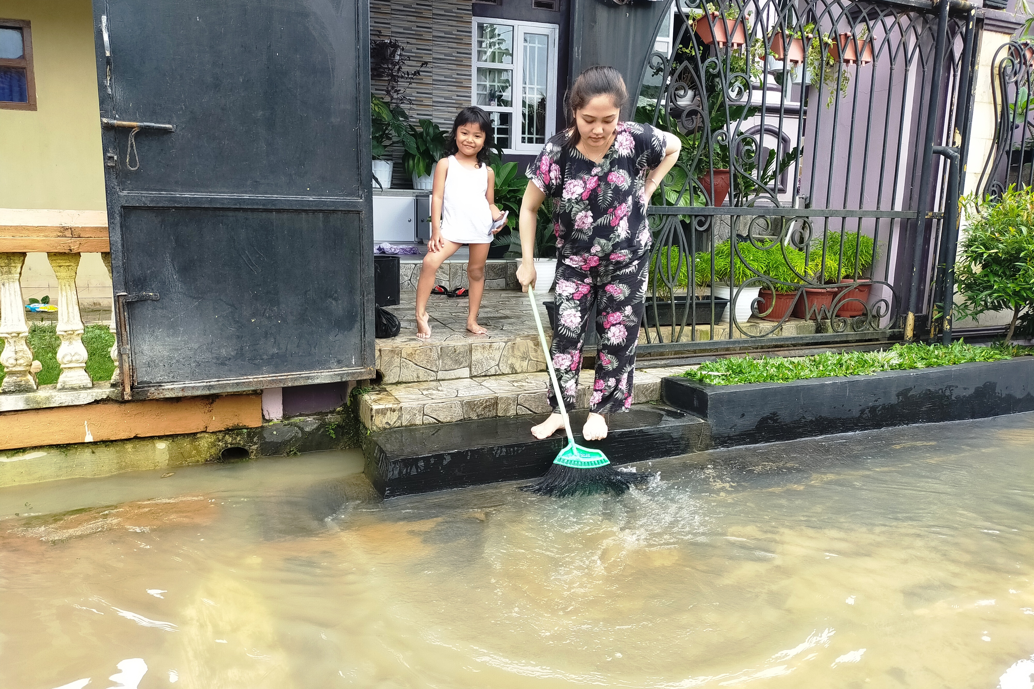 Hana Septiana, warga setempat, tengah membersihkan halaman rumah setelah banjir merendam ratusan rumah.
