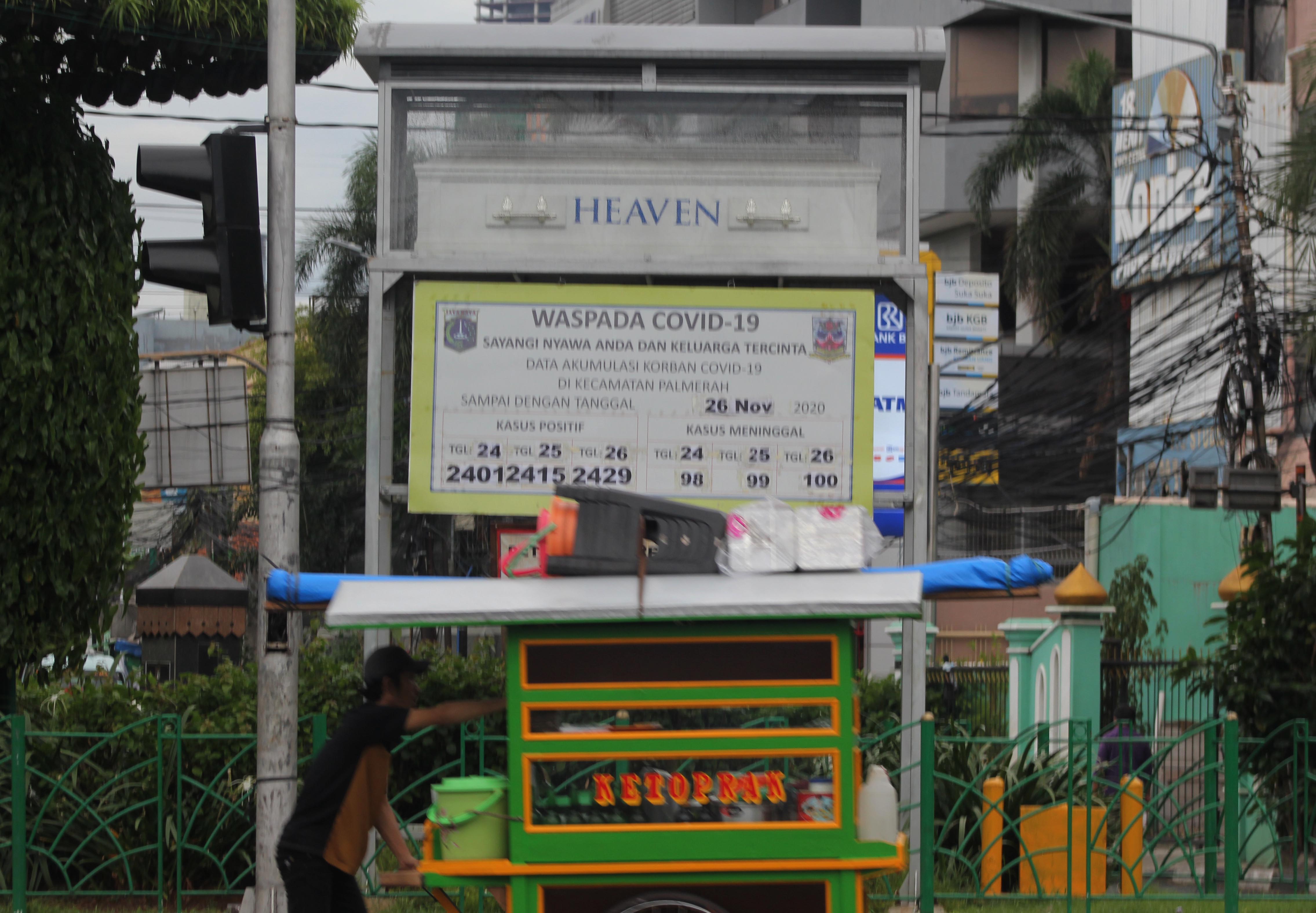 PENULARAN COVID 19 MASIH TINGGI: Pengguna jalan melintasi tugu Simbol Peringatan Bahaya covid-19 di Jalan KS Tubun, Jakarta, 