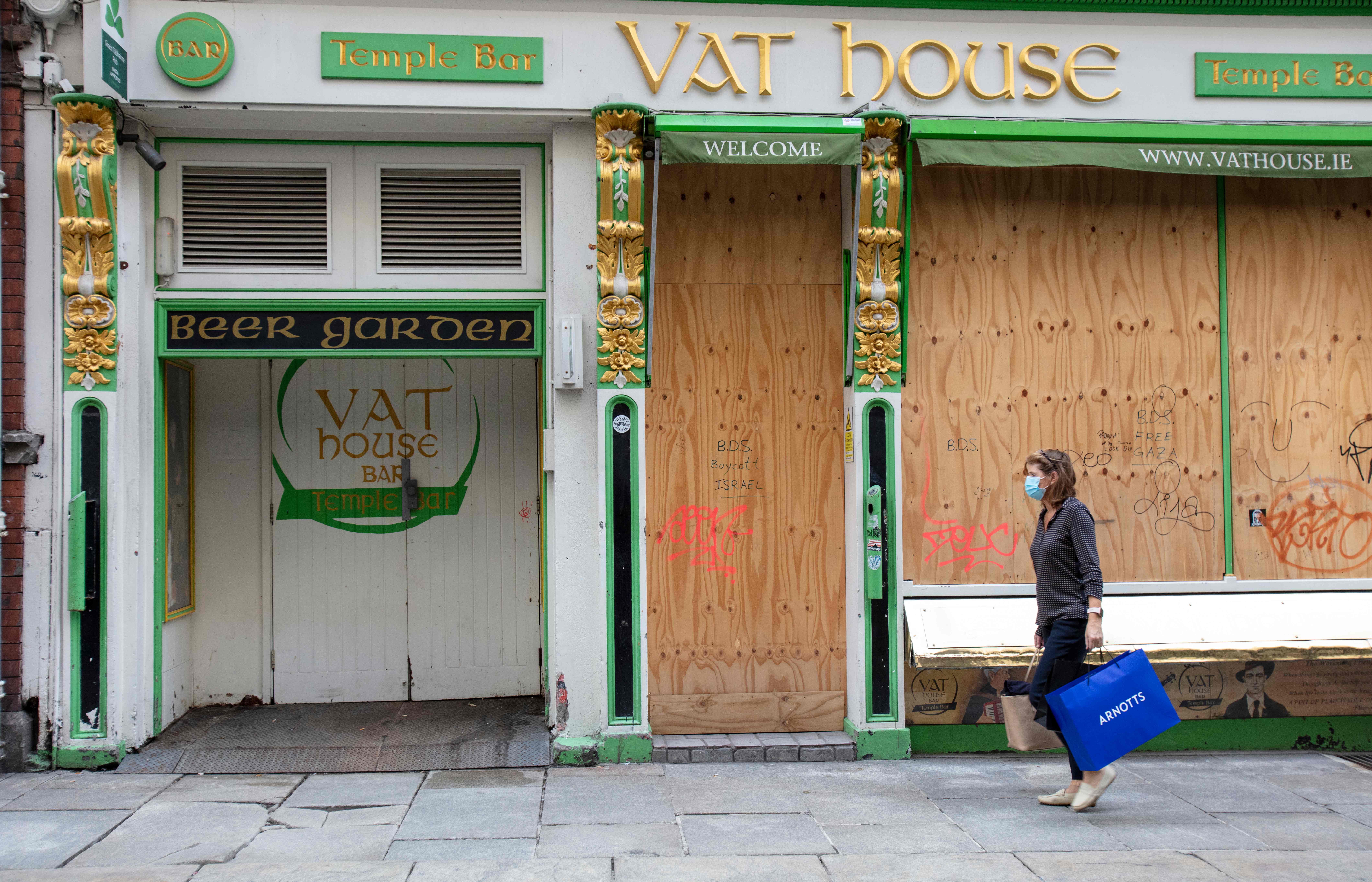 Seorang warga mengenakan masker melintas di depan bar yang tutup akibat pandemi covid-19 di Dublin, Irlandia.