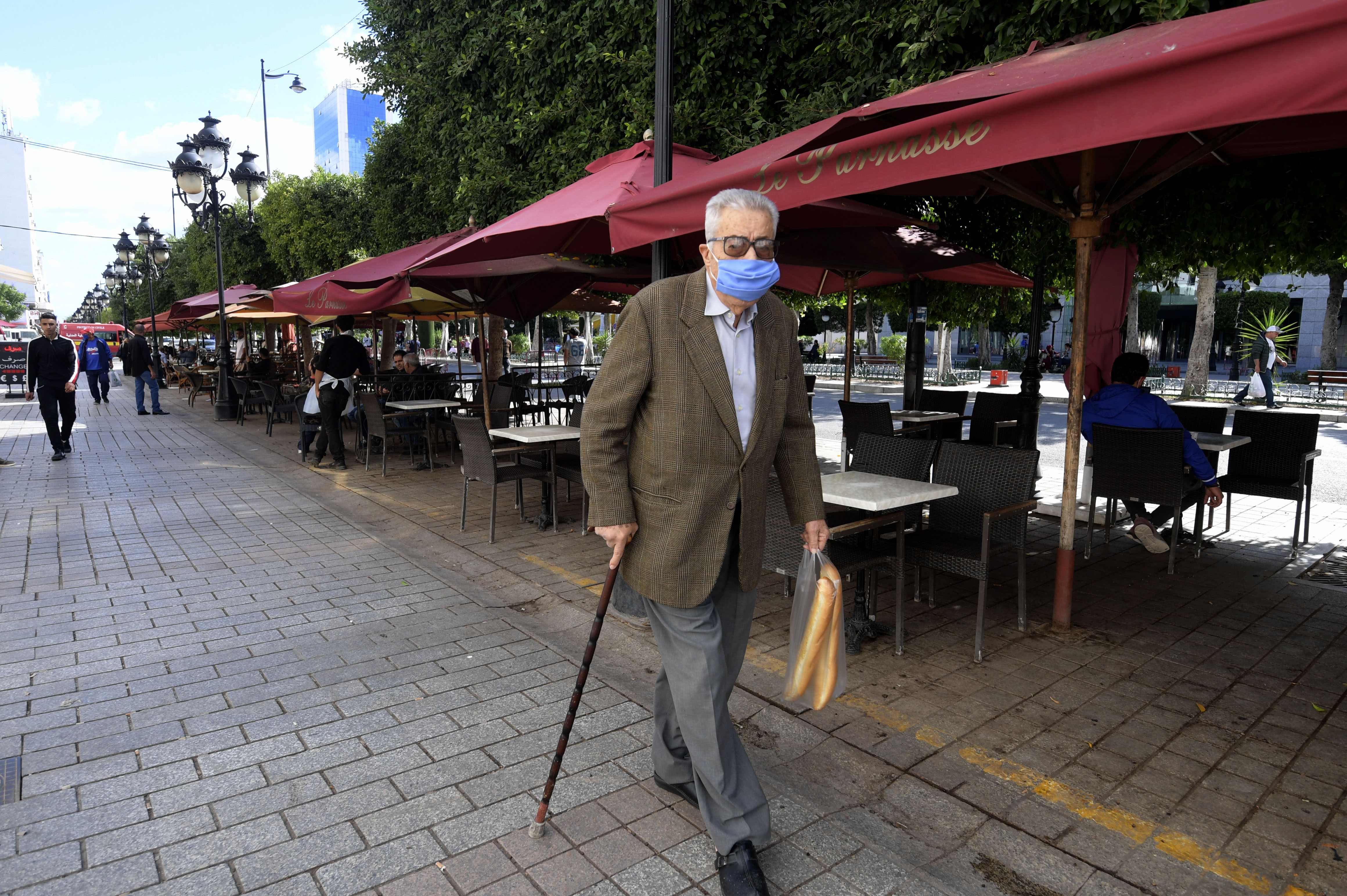 Warga yang mengenakan masker melintas di depan kafe-kafe yang tutup di Tunis, Tunisia.