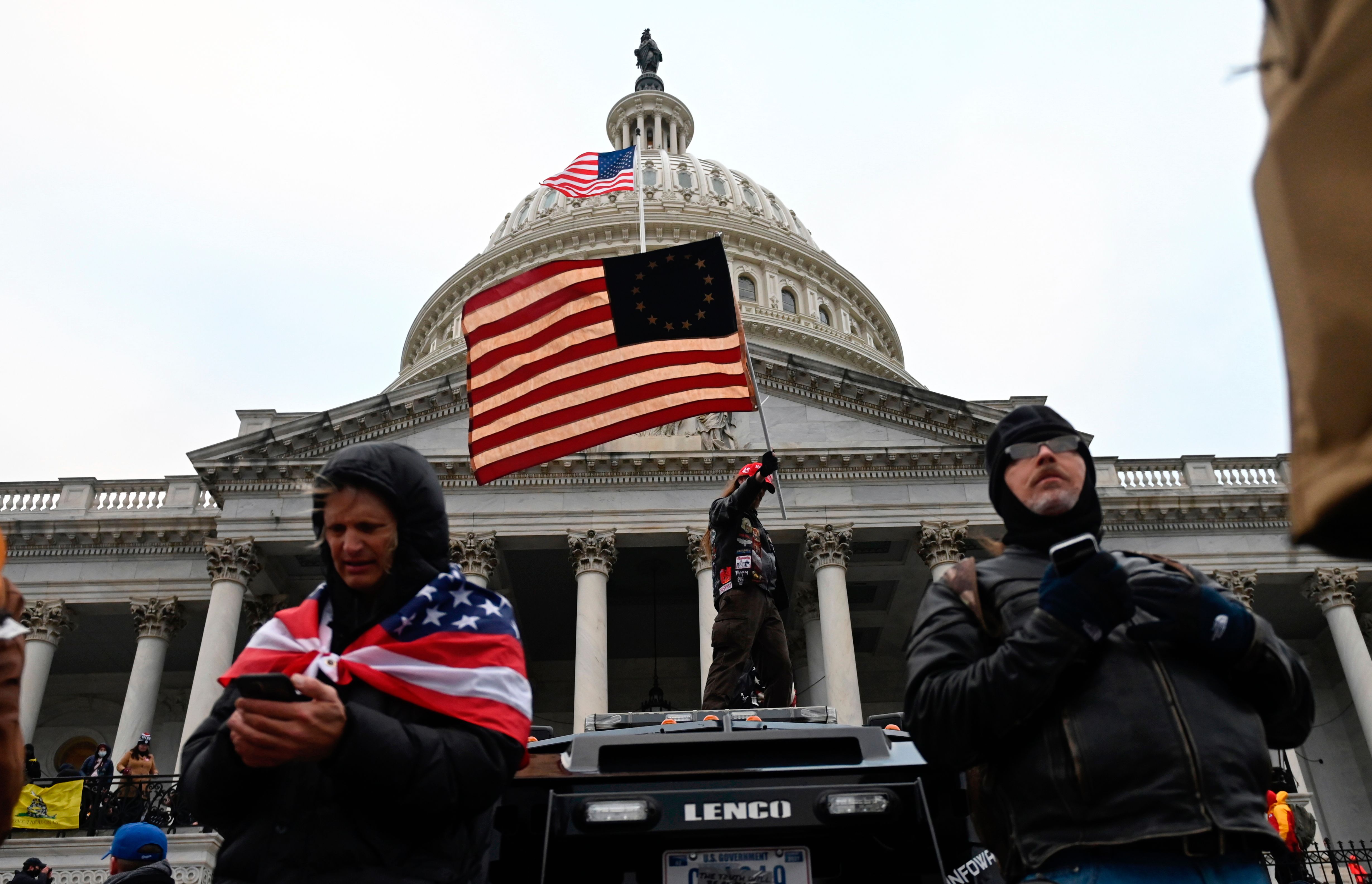 Seorang pendukung Presiden AS Donald Trump mengibarkan bendera di atas mobil polisi di depan gedung Capitol, Washington DC.