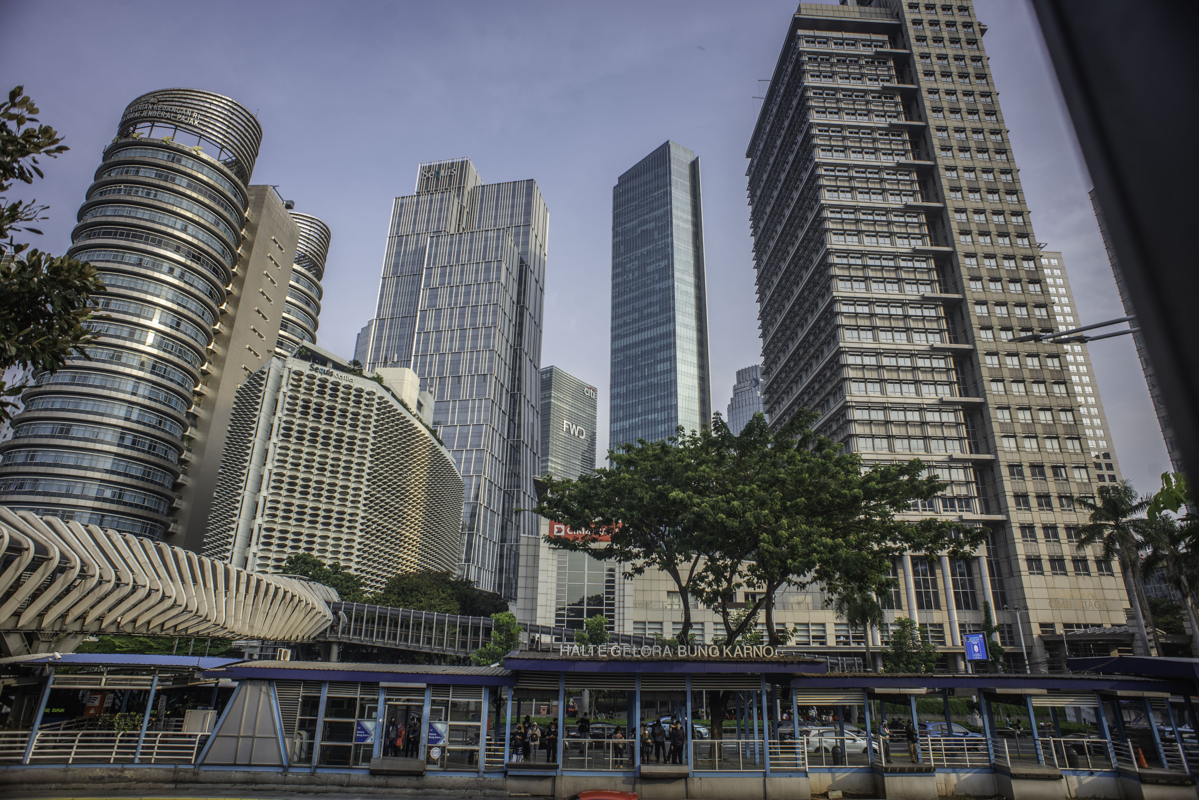 Sejumlah penumpang menunggu bus TransJakarta di Halte GBK dengan latar belakang gedung bertingkat