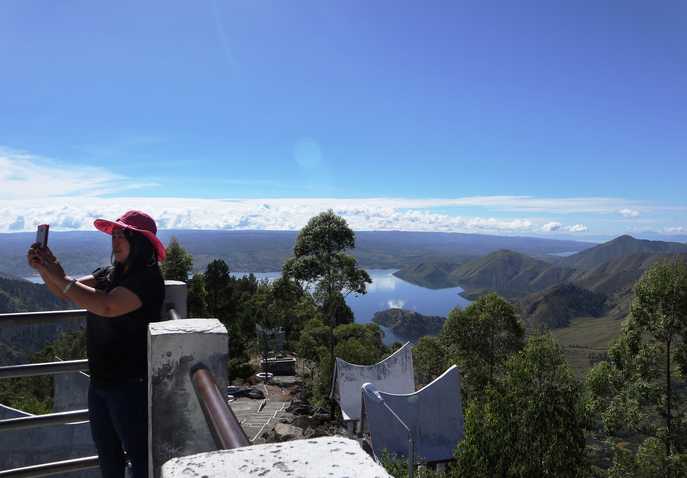 Seorang wisatawan berswafoto di menara pandang tele, kabupaten samosir dengan latar belakang kaldera Danau Toba, Kamis (28/6).