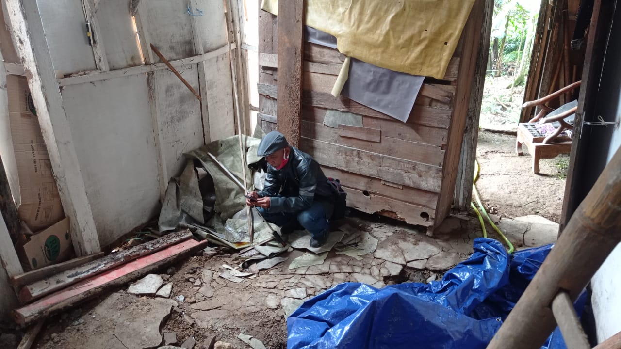 Warga Ragatunjung, sedang menunjukan tanah bergerak yang menyebabkan lantai rumahnya turun.