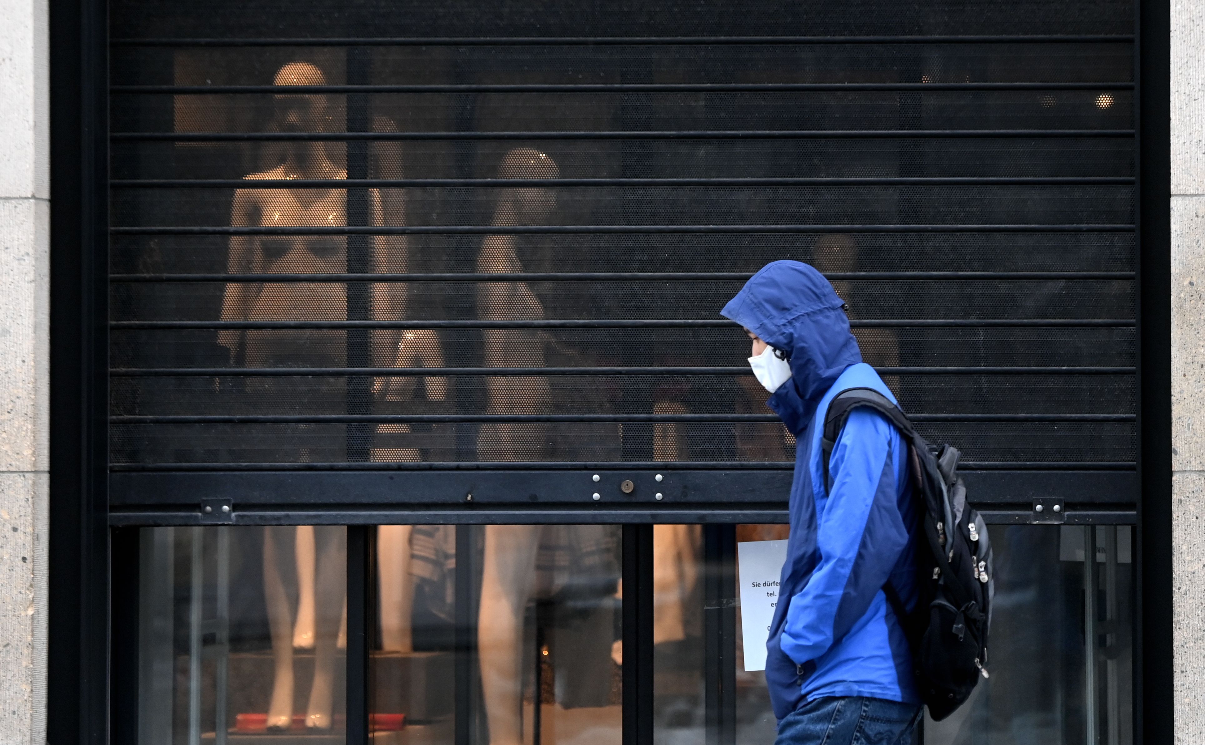 Warga mengenakan masker melintas di depan sebuah toko yang tutup di Muenchen, Jerman.