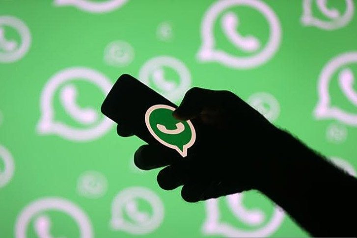 Ilustrasi - Seorang pria dengan smartphonenya di depan logo Whatsapp. 