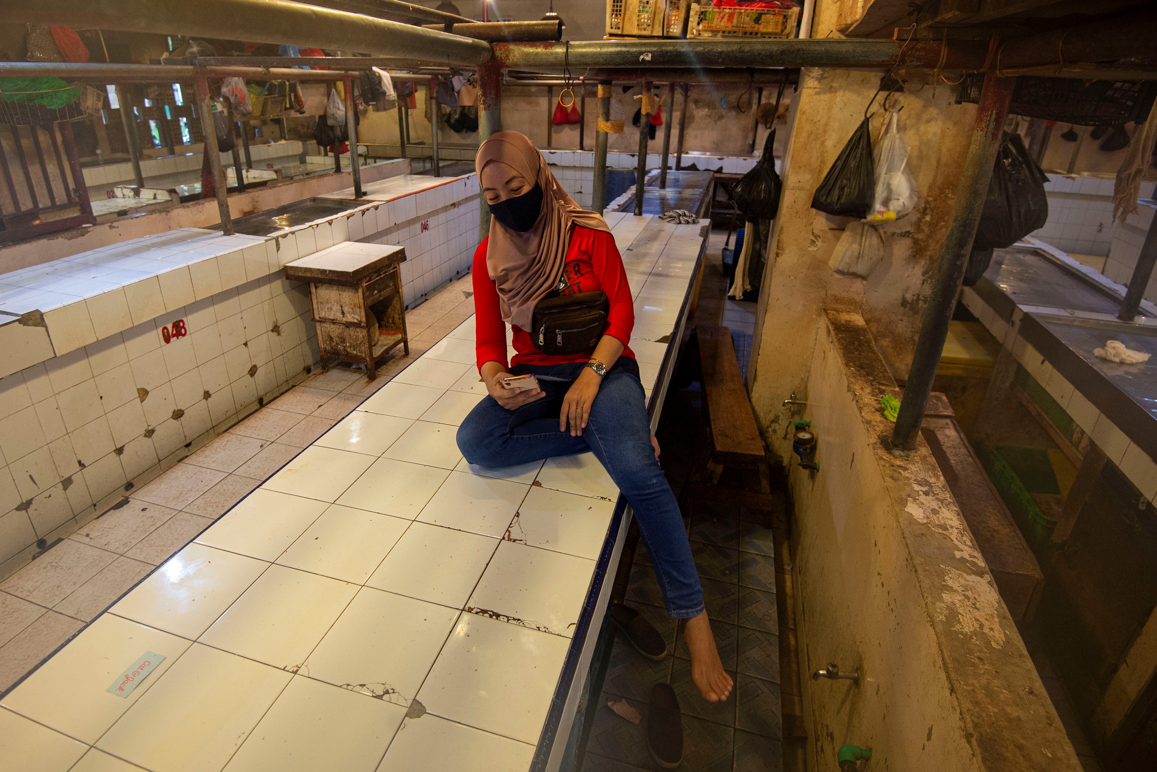 Pedagang menggunakan telepon pintarnya di los daging yang sepi akibat aksi mogok di Pasar Senen, Jakarta, Rabu (20/1).