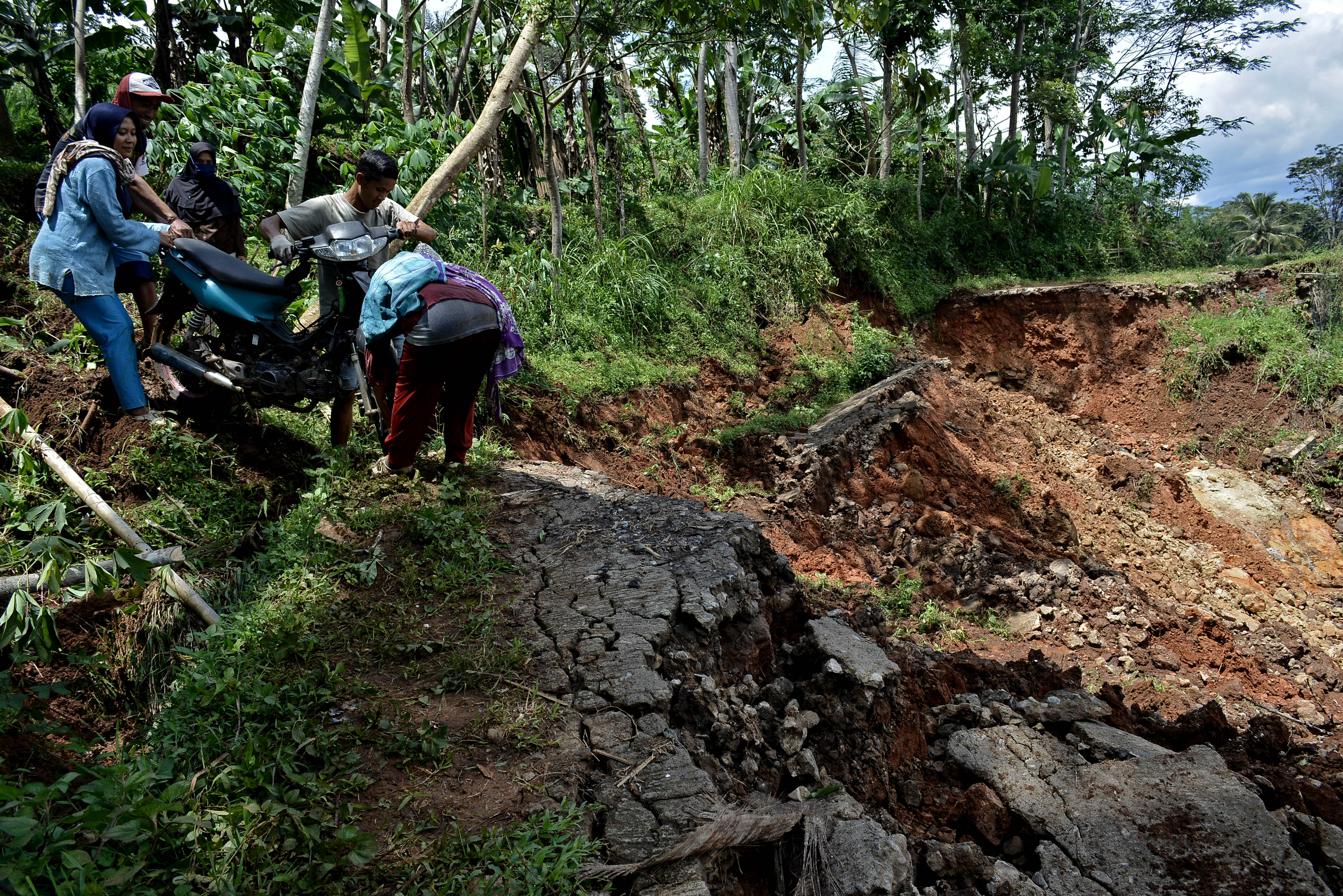JALAN PEDESAAN LONGSOR: Warga mengangkat kendaraan roda dua saat melintasi jalan yang terdampak longsor, di Singajaya, Kabupaten Garut.