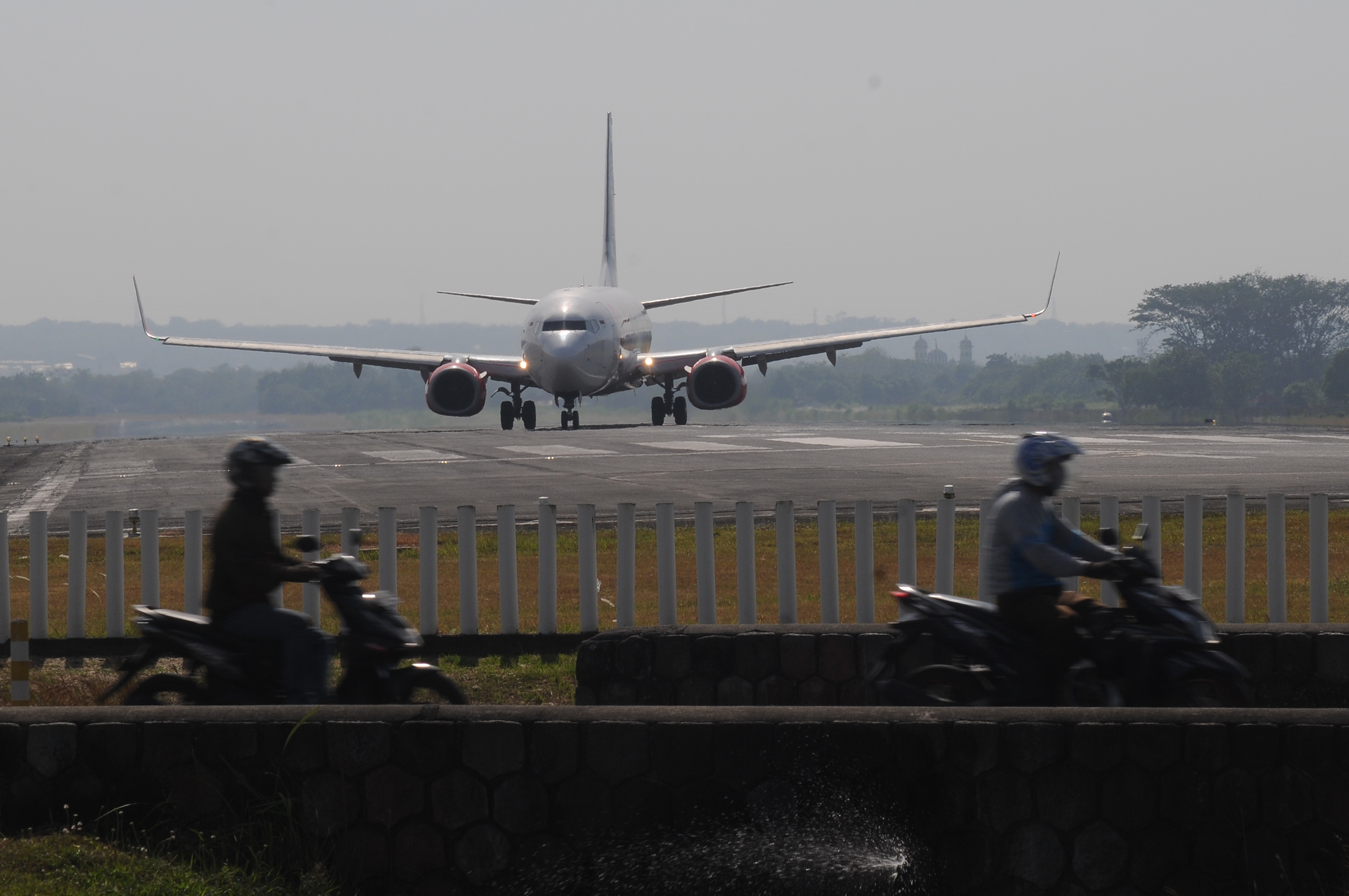 Sejumlah pengendara motor melintas dengan latar belakang pesawat komersial yang akan lepas landas di Bandara Adi Soemarmo, Boyolali, Jateng.