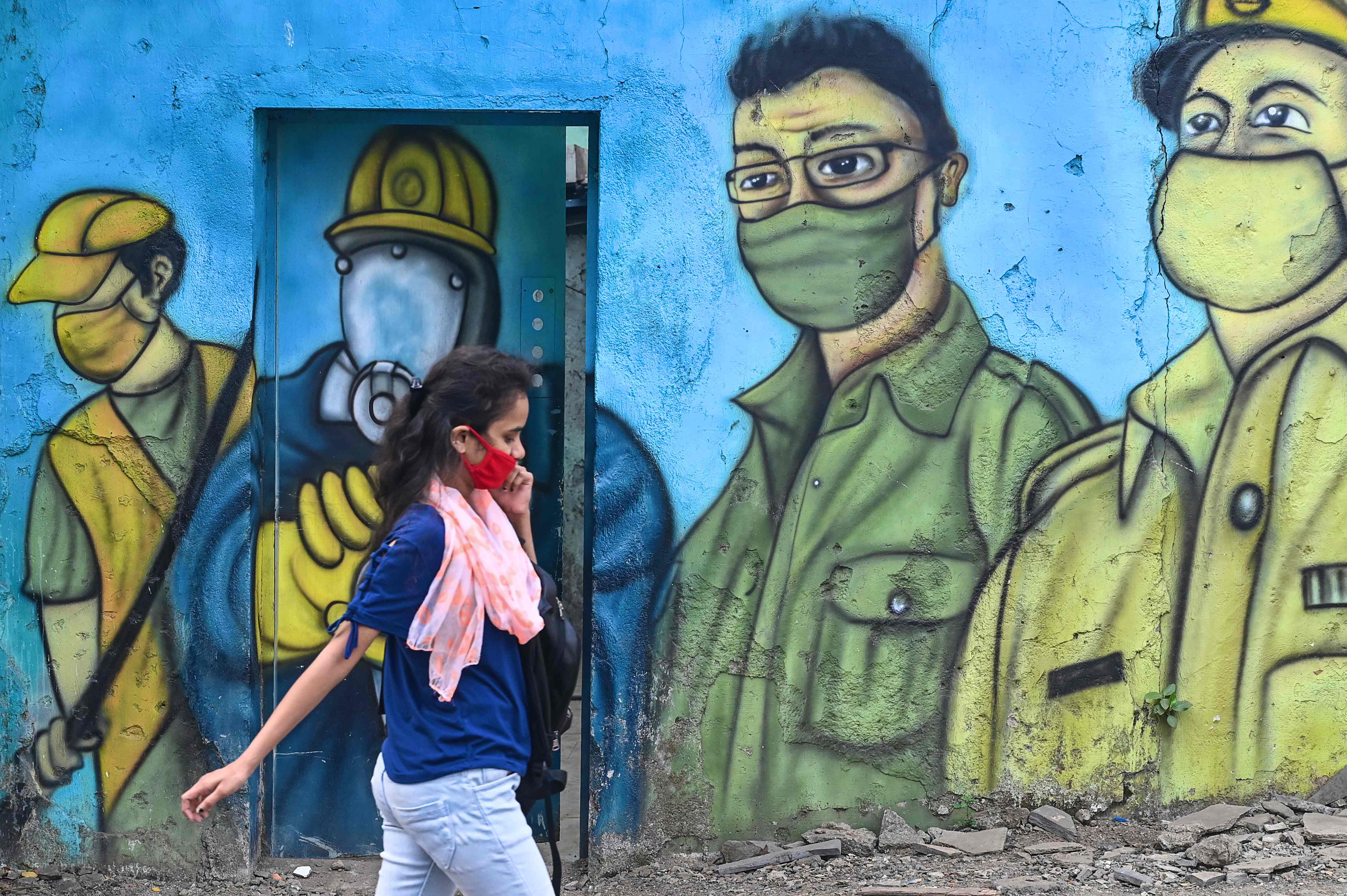 Seorang warga yang mengenakan masker melintas tembok yang bergambar mural 'prajurit anti-Covid-19' di Mumbai, India.