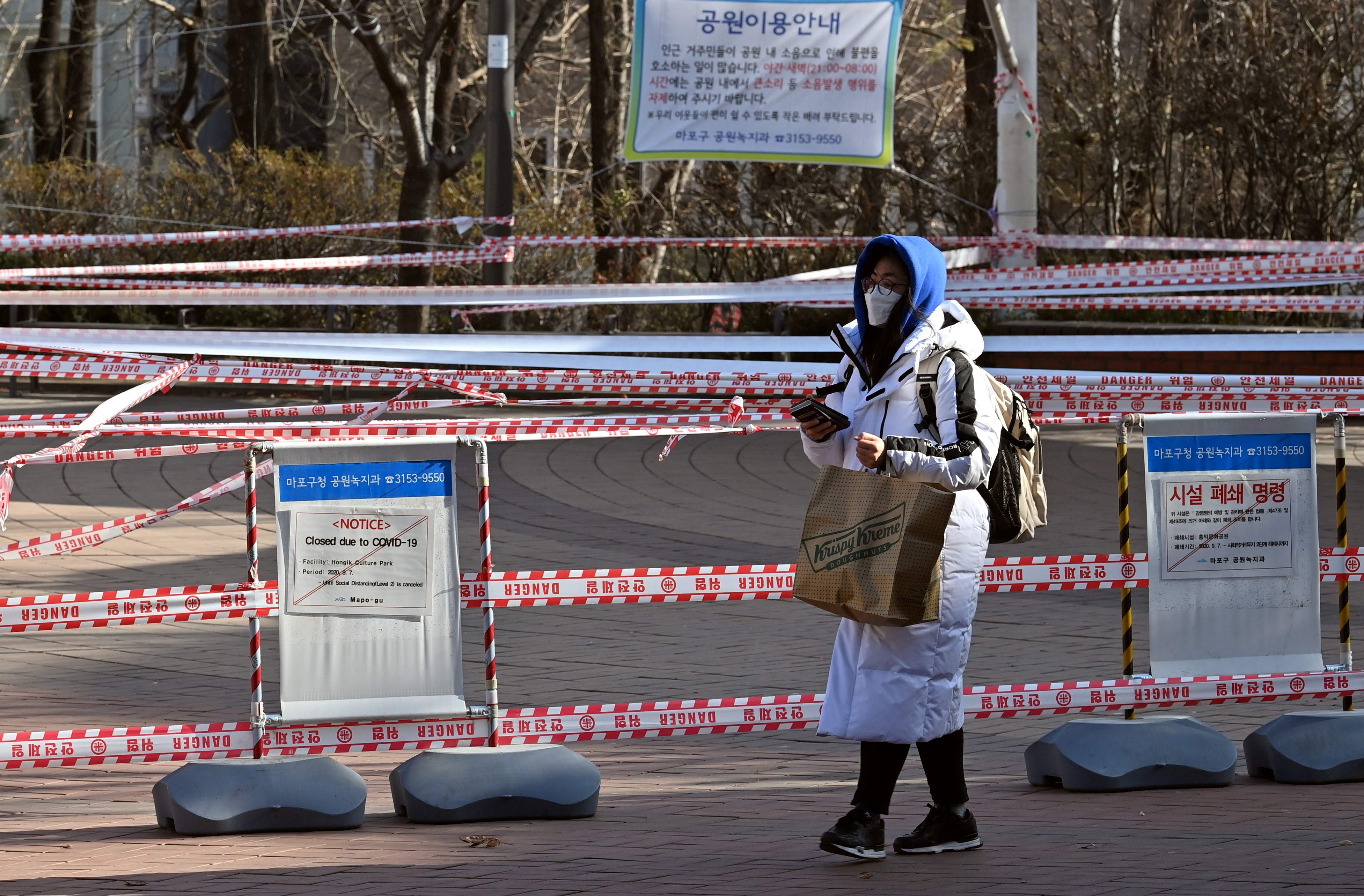 Seorang wanita yang mengenakan masker melintasi area yang dibatasi untuk cegah kerumunan di Kota Seoul, Korea Selatan.