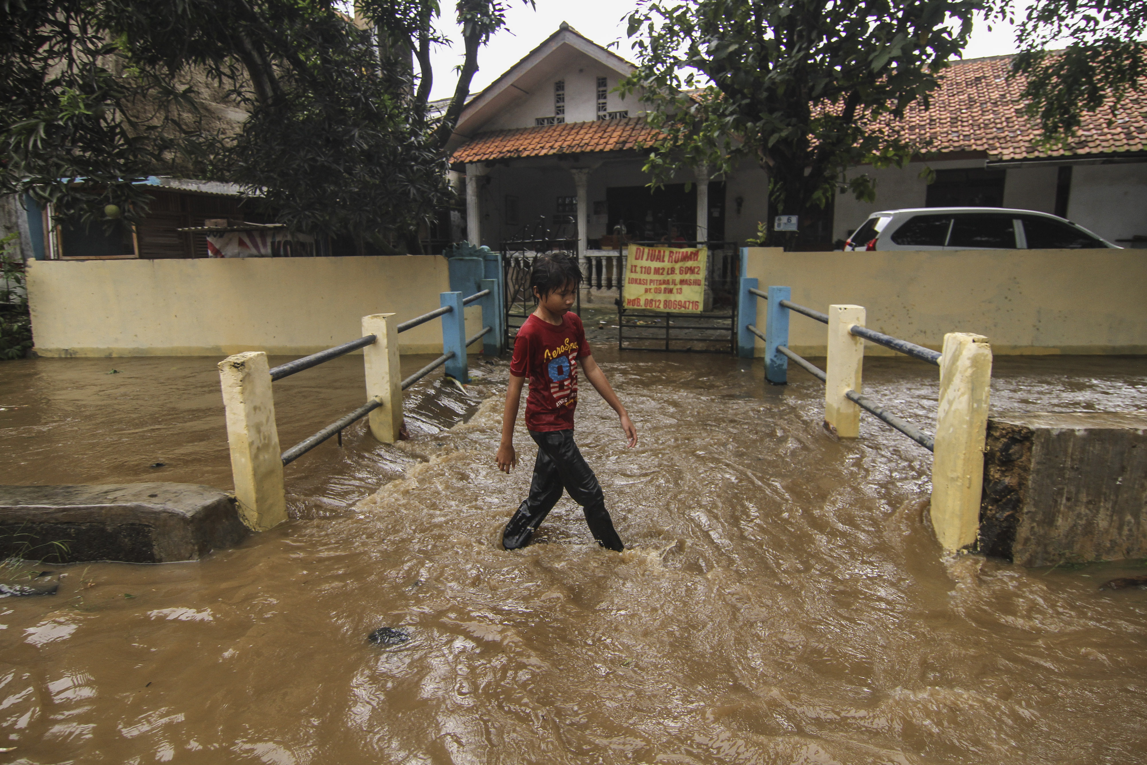 Seorang anak melintasi banjir dekat kali yang meluap di wilayah Depok, Jawa Barat. 