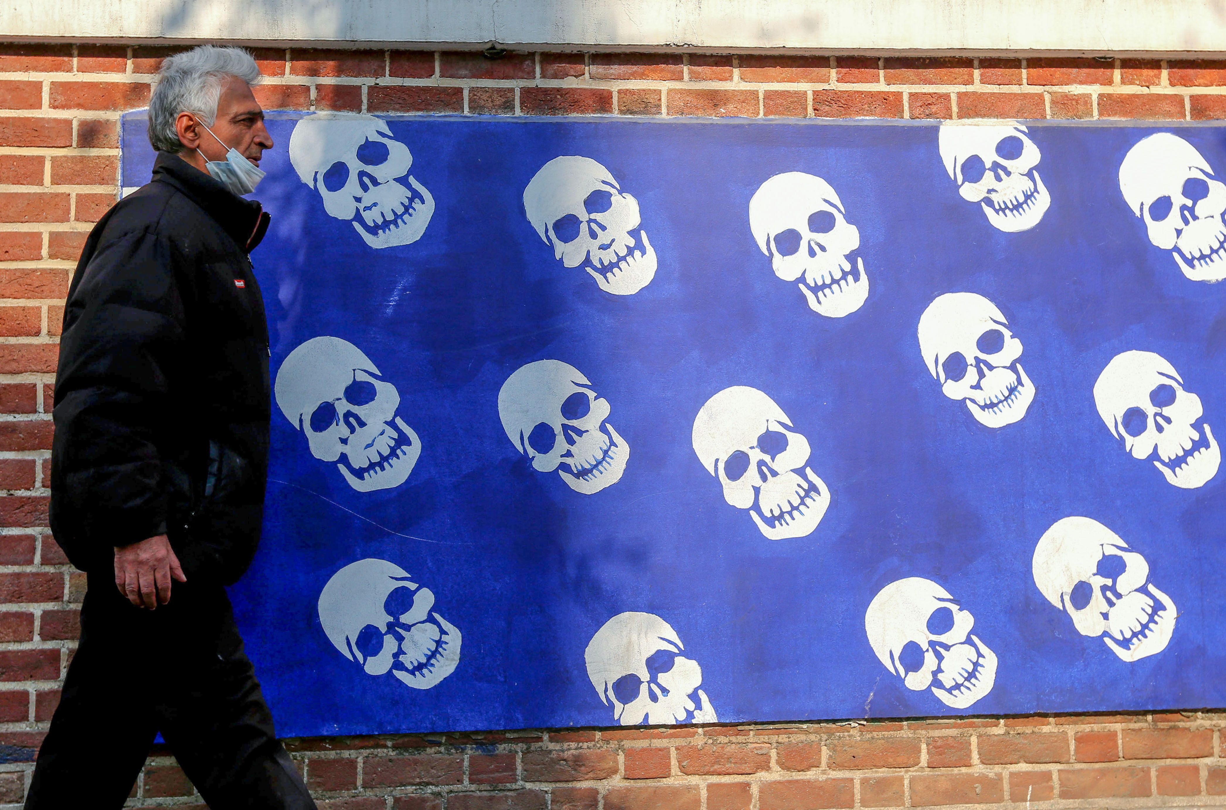 Seorang warga Iran mengenakan masker saat melintasi Kedutaan Besar Amerika Serikat di Teheran, Desember 2020.