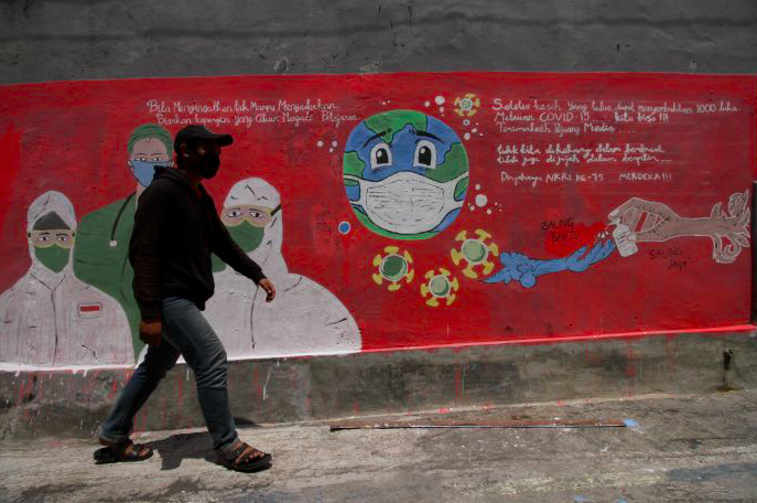 Seorang warga melintas di depan mural kampanye untuk melawan covid-19.