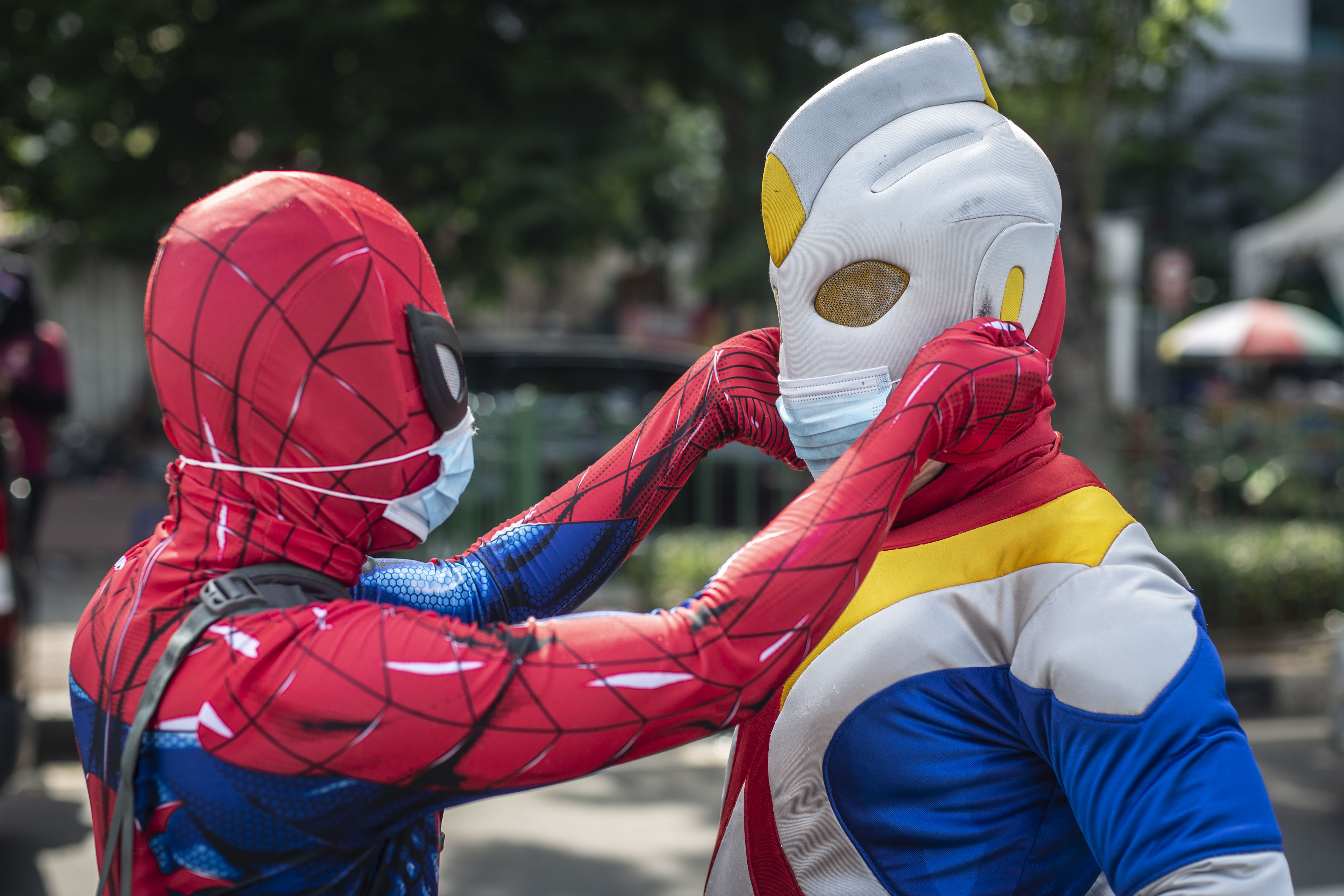 Pekerja seni berkostum Spiderman merapikan masker tokoh berkostum Ultraman saat sosialisasi Jakarta Bermasker di Jakarta, Kamis (4/2).