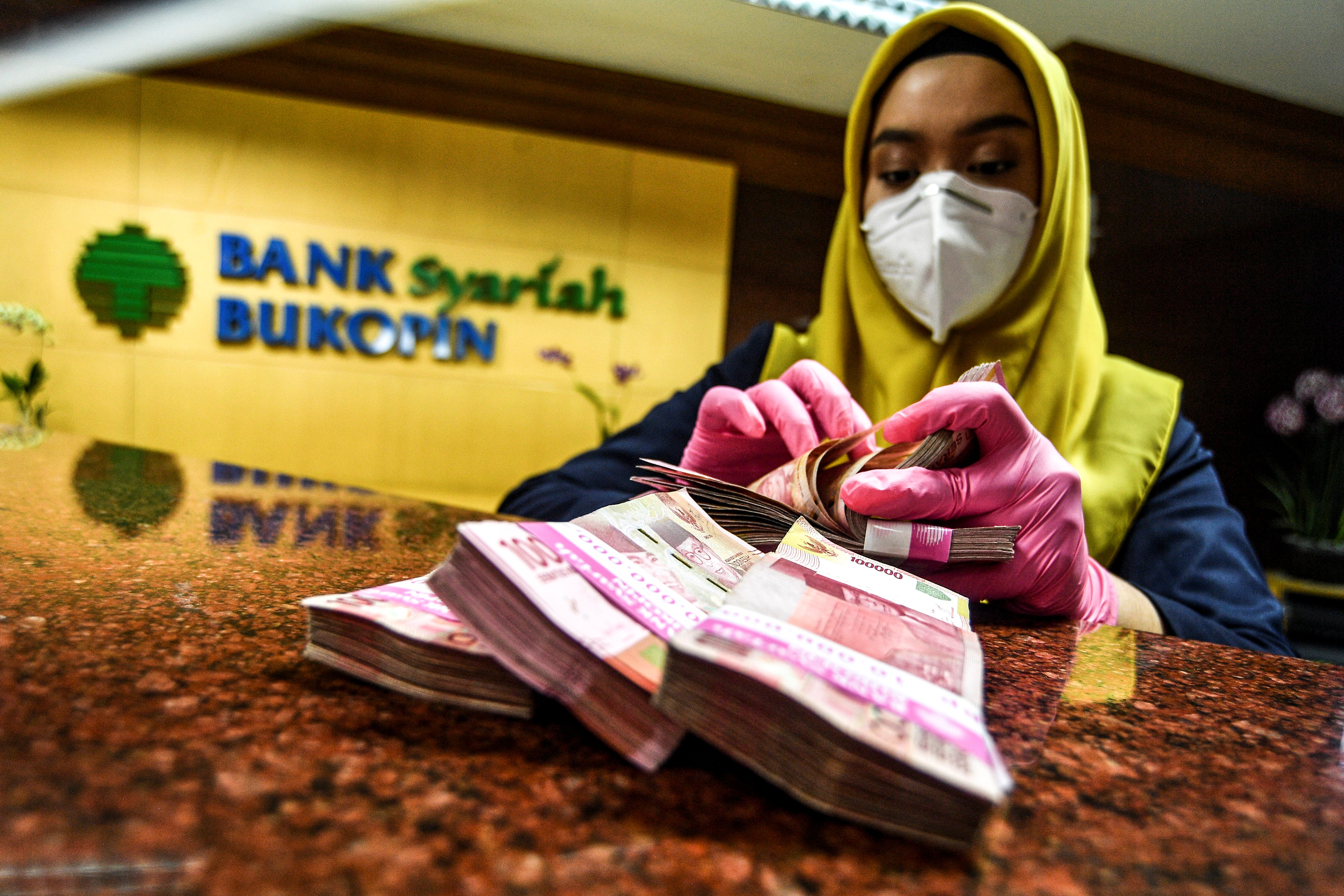Karyawan menghitung uang pecahan Rp100 ribu dari setoran nasabah di Bank Bukopin Syariah, Jakarta, beberapa waktu lalu.