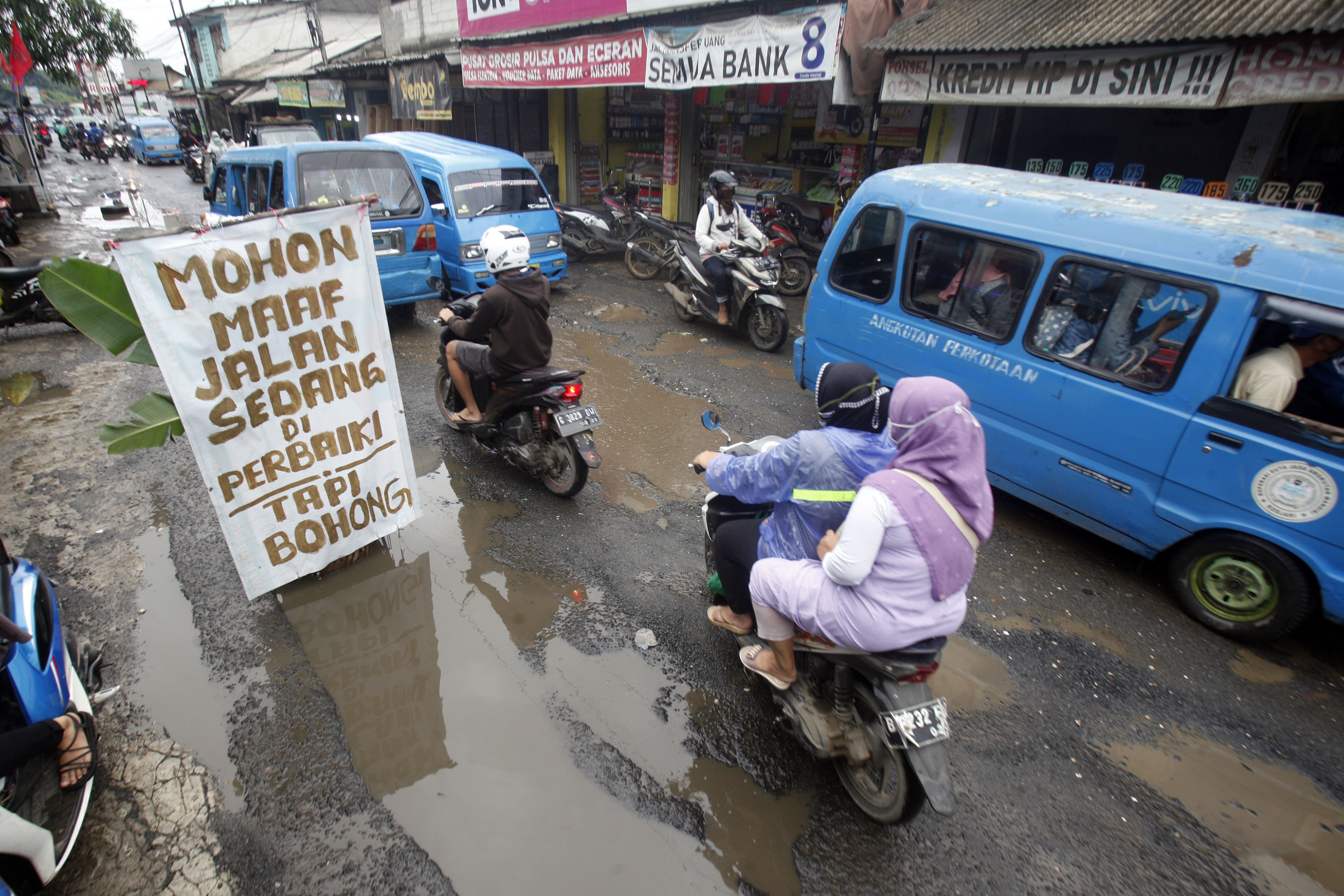 Pengendara melintasi jalan yang rusak dan tergenang air di jalan penghubung antara Kabupaten Bogor dan Kota Depok, di Bojong Gede.