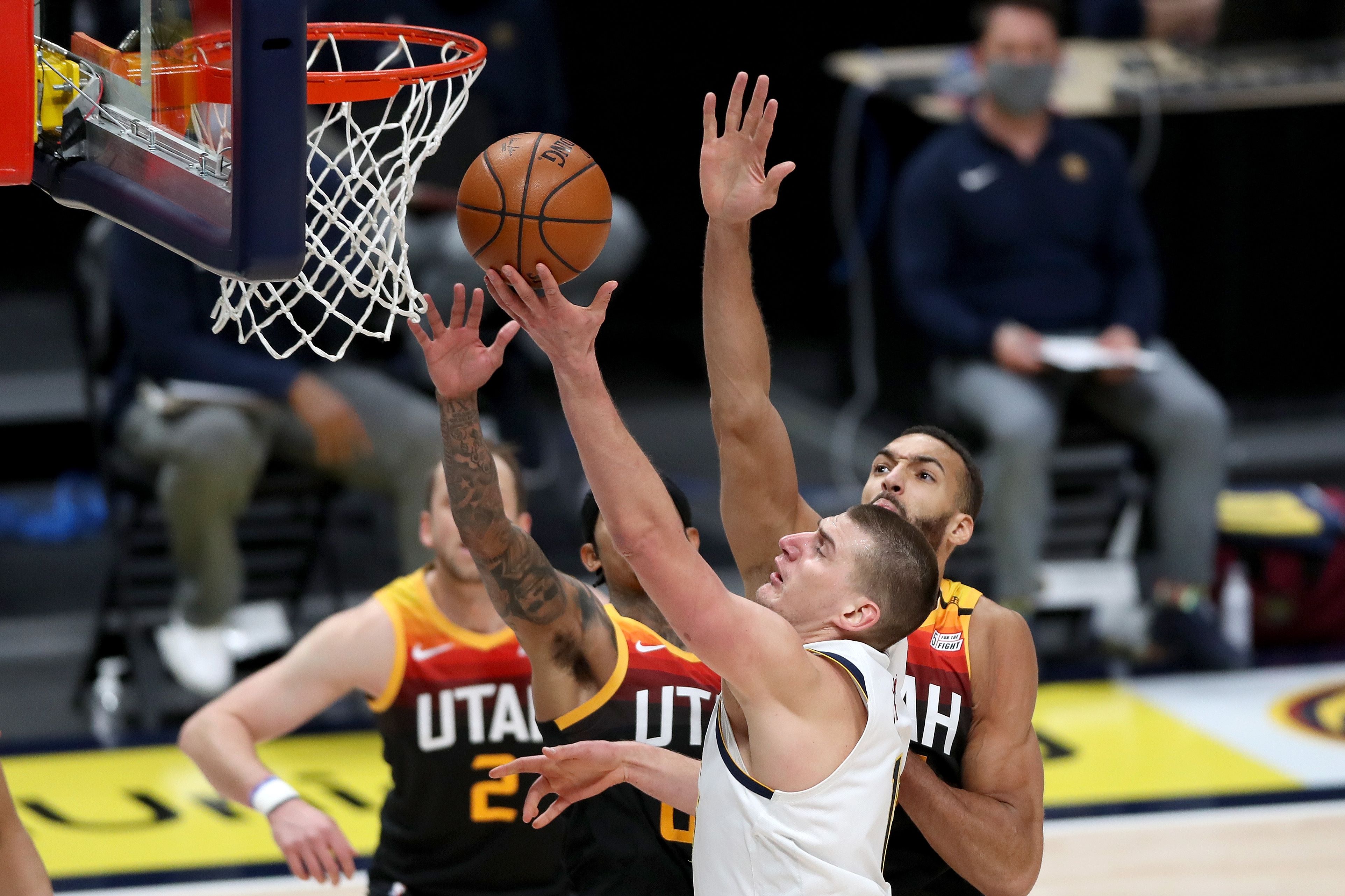 Pemain Denver Nuggets Nikola Jokic melakukan layup melewati dua pemain Utah Jazz di laga NBA.