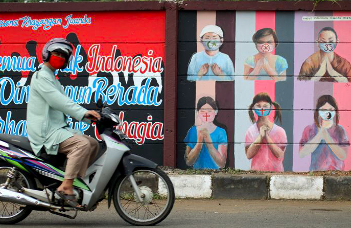 Warga melintas dekat mural bergambar simbol orang berdoa menggunakan masker yang mewakili umat beragama di Indonesia di Jalan Juanda, Depok.