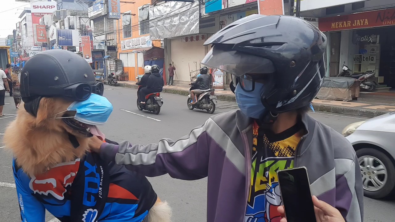 Wawa (kanan) bersama anjingnya, Joy, yang dipakaikan masker, helm, dan kaca mata hitam di Tasikmalaya.