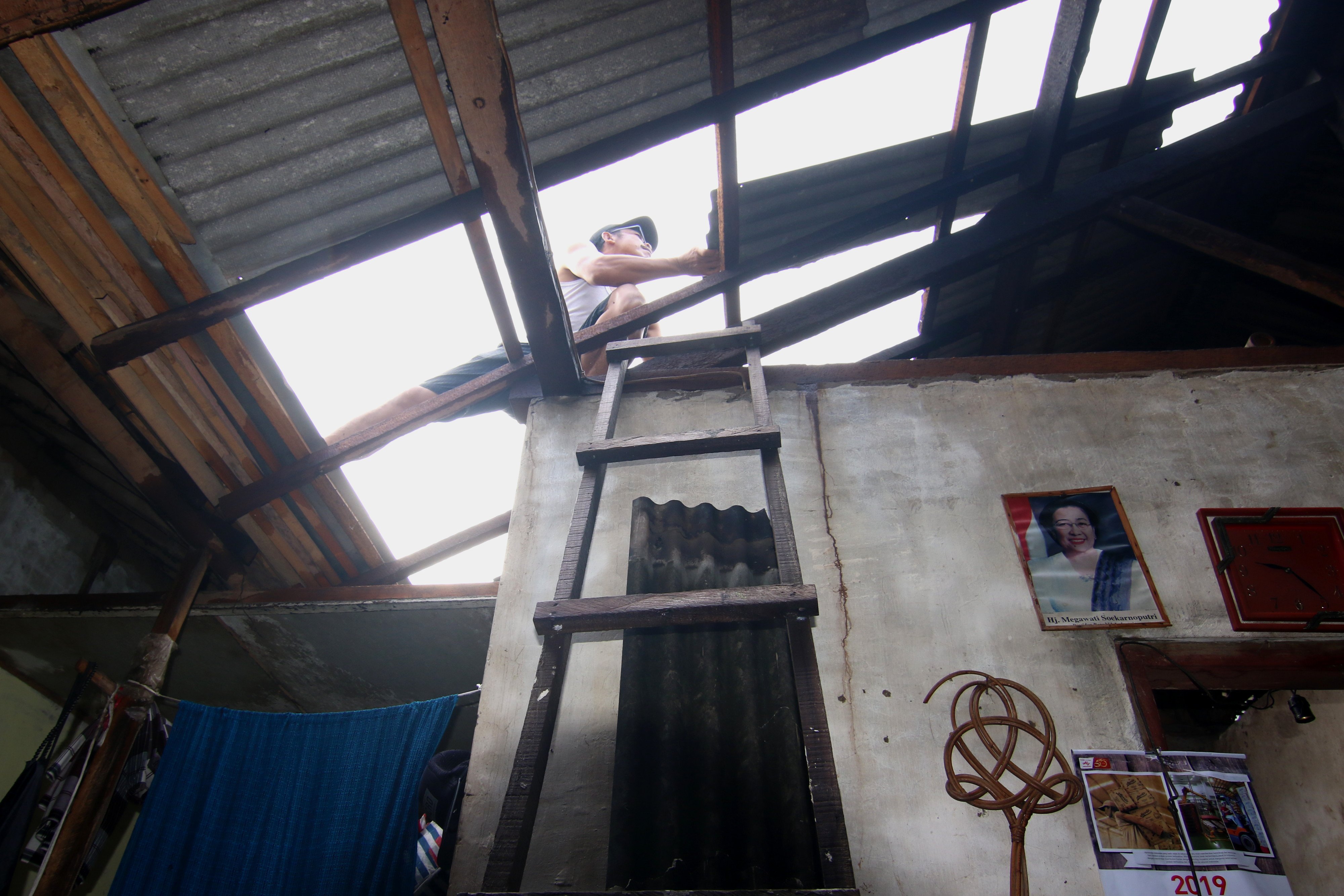 Warga membenahi atap rumah yang rusak akibat angin puting beliung di Sarimulyo, Cluring, Banyuwangi, Jawa Timur.