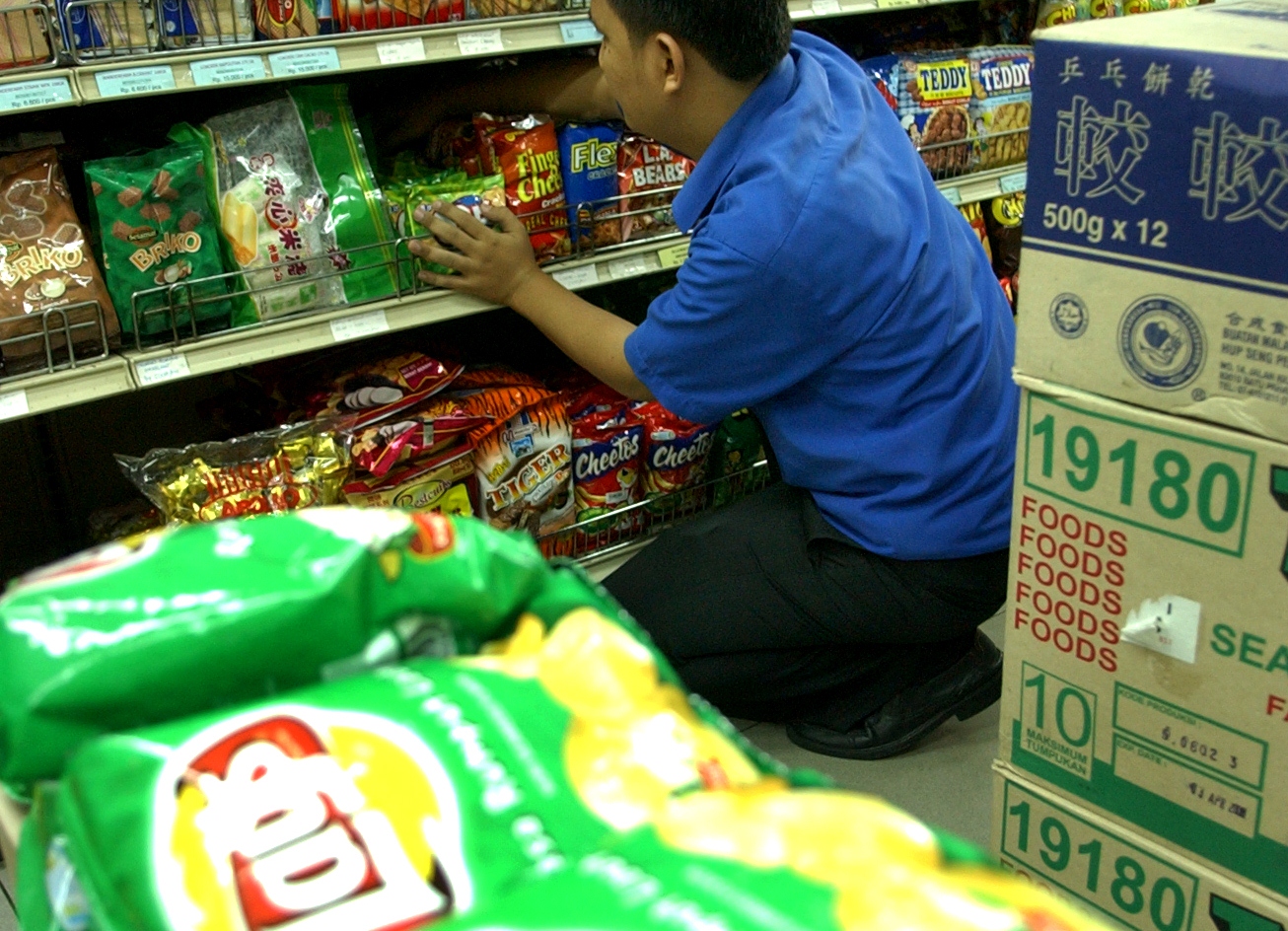 Pegawai minimarket menata produk makanan ringan