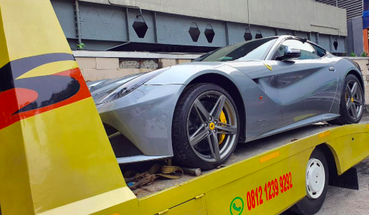 Petugas memindahkan barang bukti berupa satu unit mobil Ferrari Tipe F12 Berlinetta warna abu-abu metalik nomor polisi B 15 TRM.