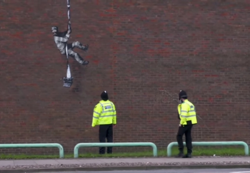 Dua polisi memperhatikan grafiti tahanan kabur karya Banksy.