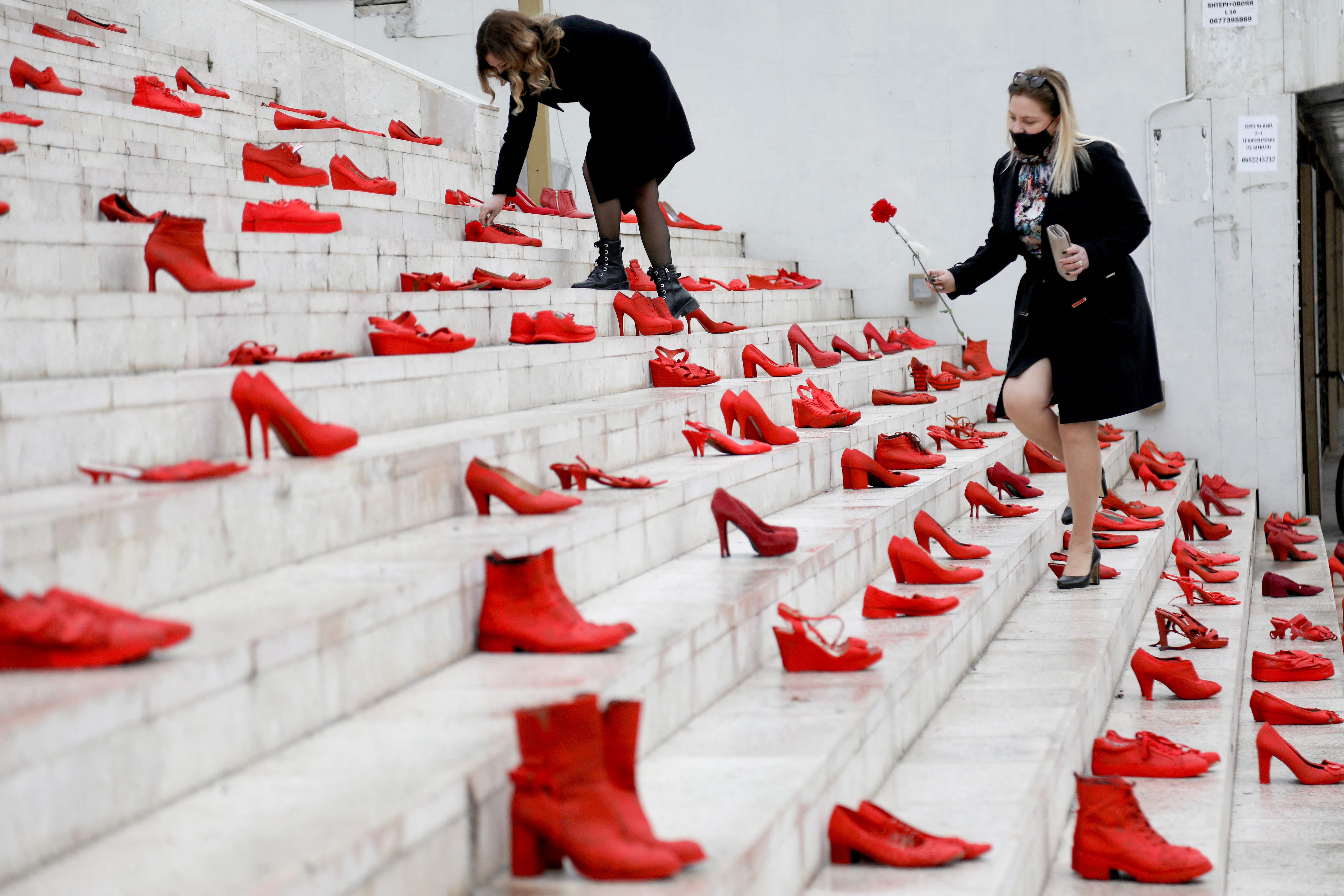 Perempuan meletakkan bunga di instalasi sepatu merah perempuan sebagai simbol untuk mengecam kekerasan terhadap perempuan