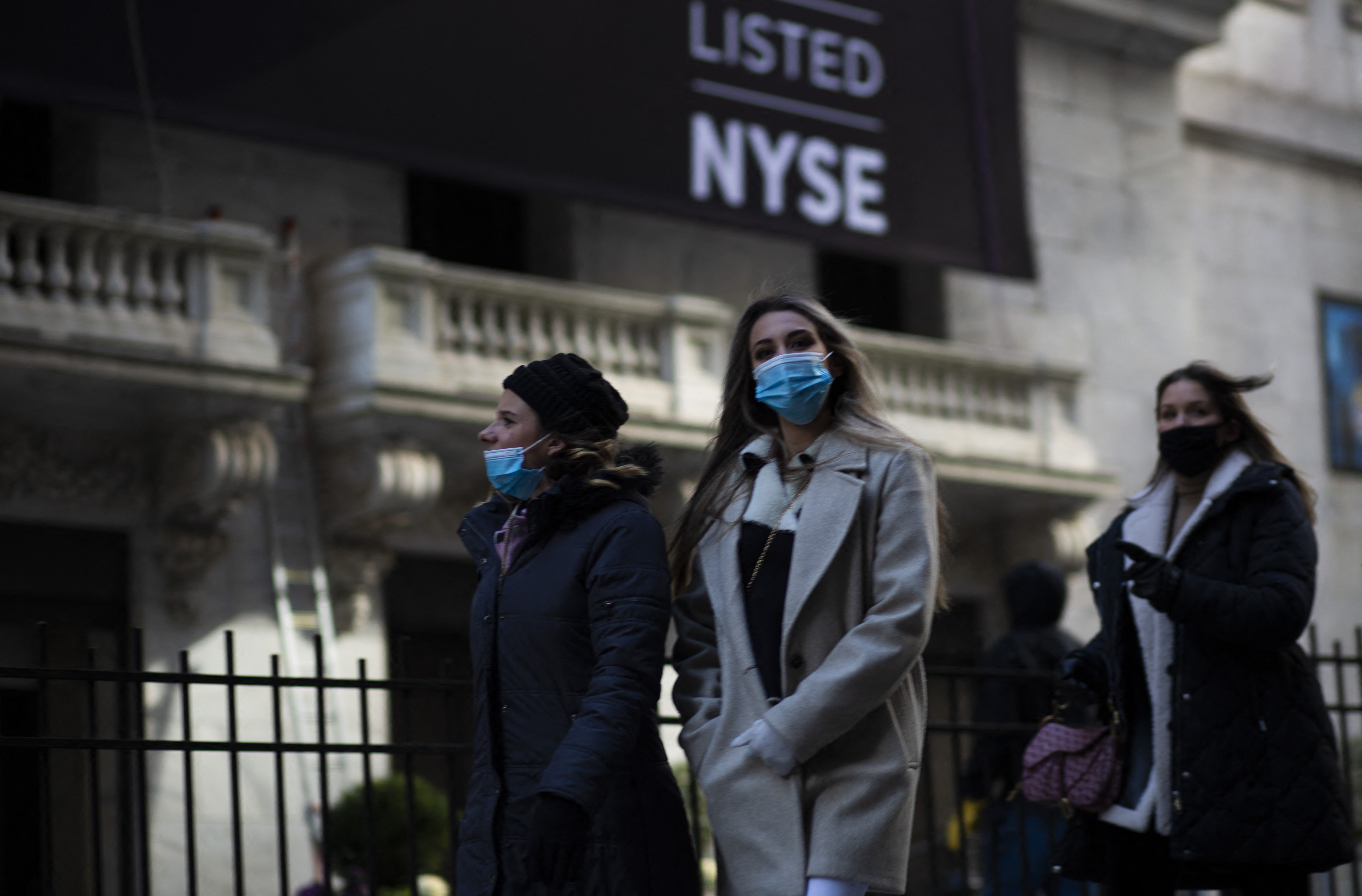 Sejumlah perempuan memakai masker berjalan di depan gedung New York Stock Exchange, Wall Street, New York, Senin (8/2/2021).
