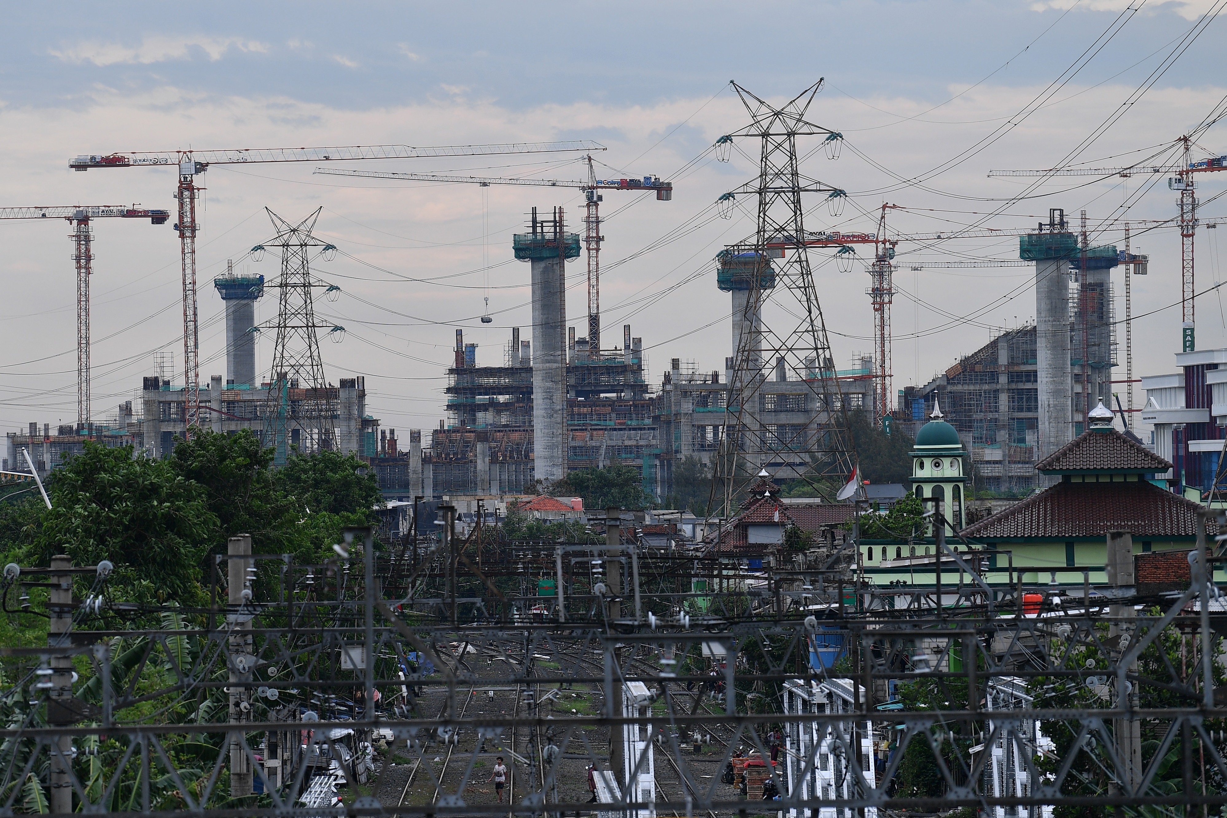 Warga beraktivitas di antara rel kereta berlatar belakang pembangunan Jakarta International Stadium di Jakarta Utara, beberapa waktu lalu.
