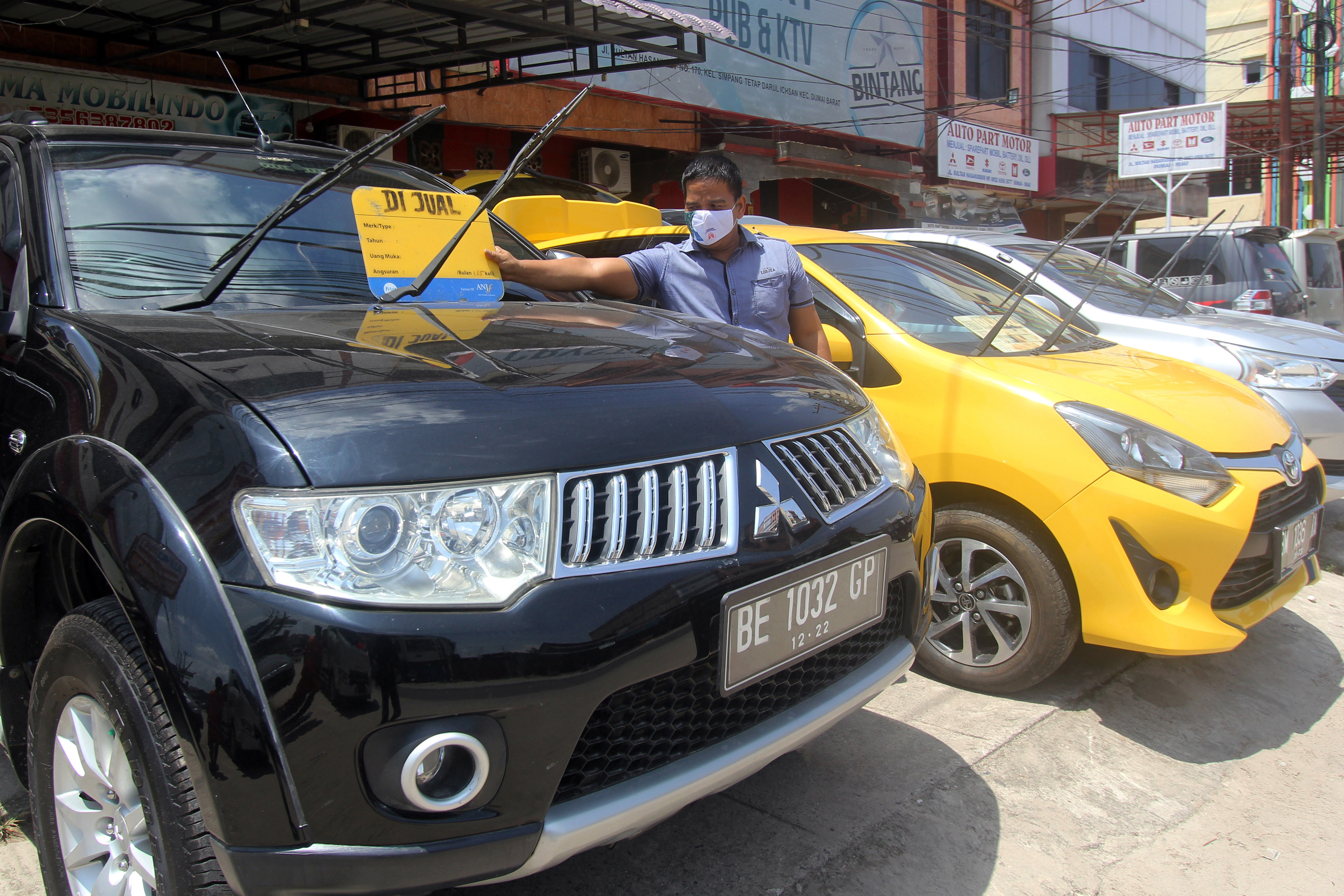 Pemilik toko meletakkan papan tanda dijual sebuah mobil bekas pakai di Dumai, Riau, Senin (22/3/2021).