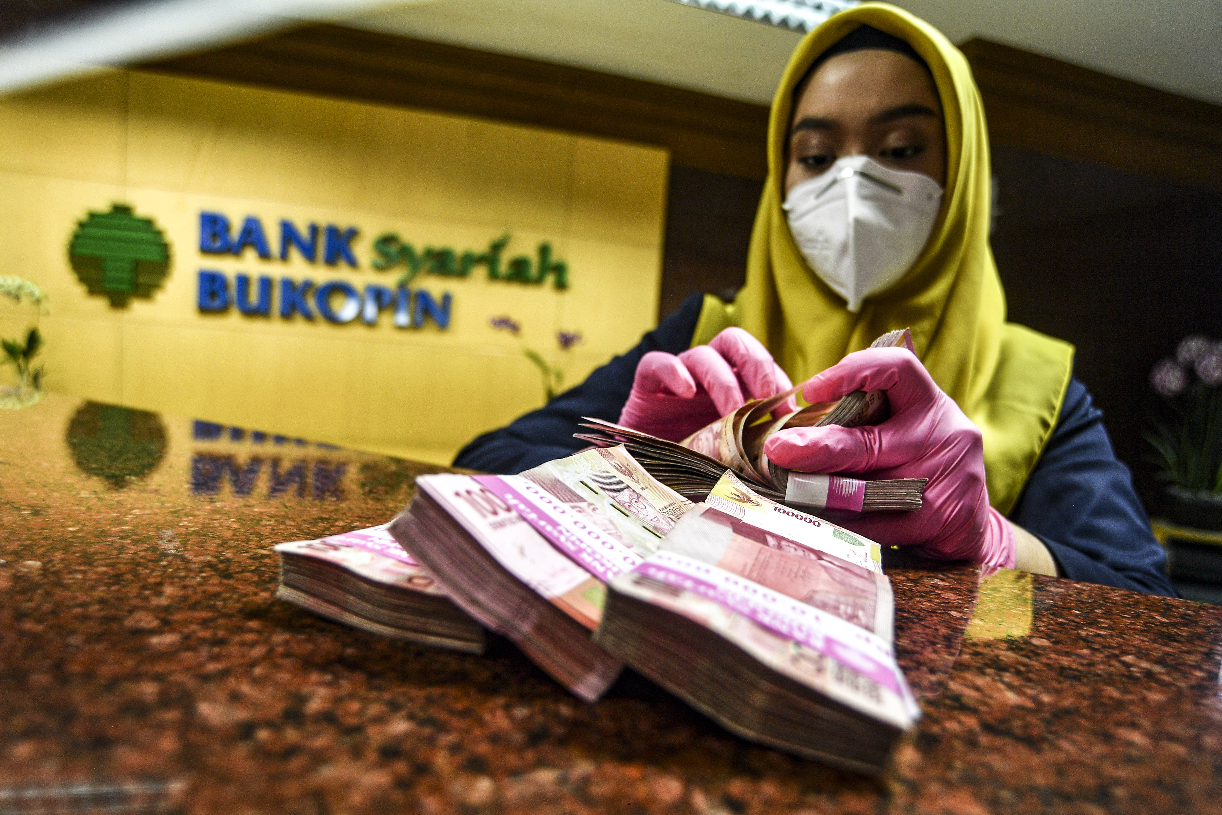 Karyawan menghitung uang pecahan Rp100 ribu dari setoran nasabah di Bank Bukopin Syariah, Jakarta, Kamis (11/2).
