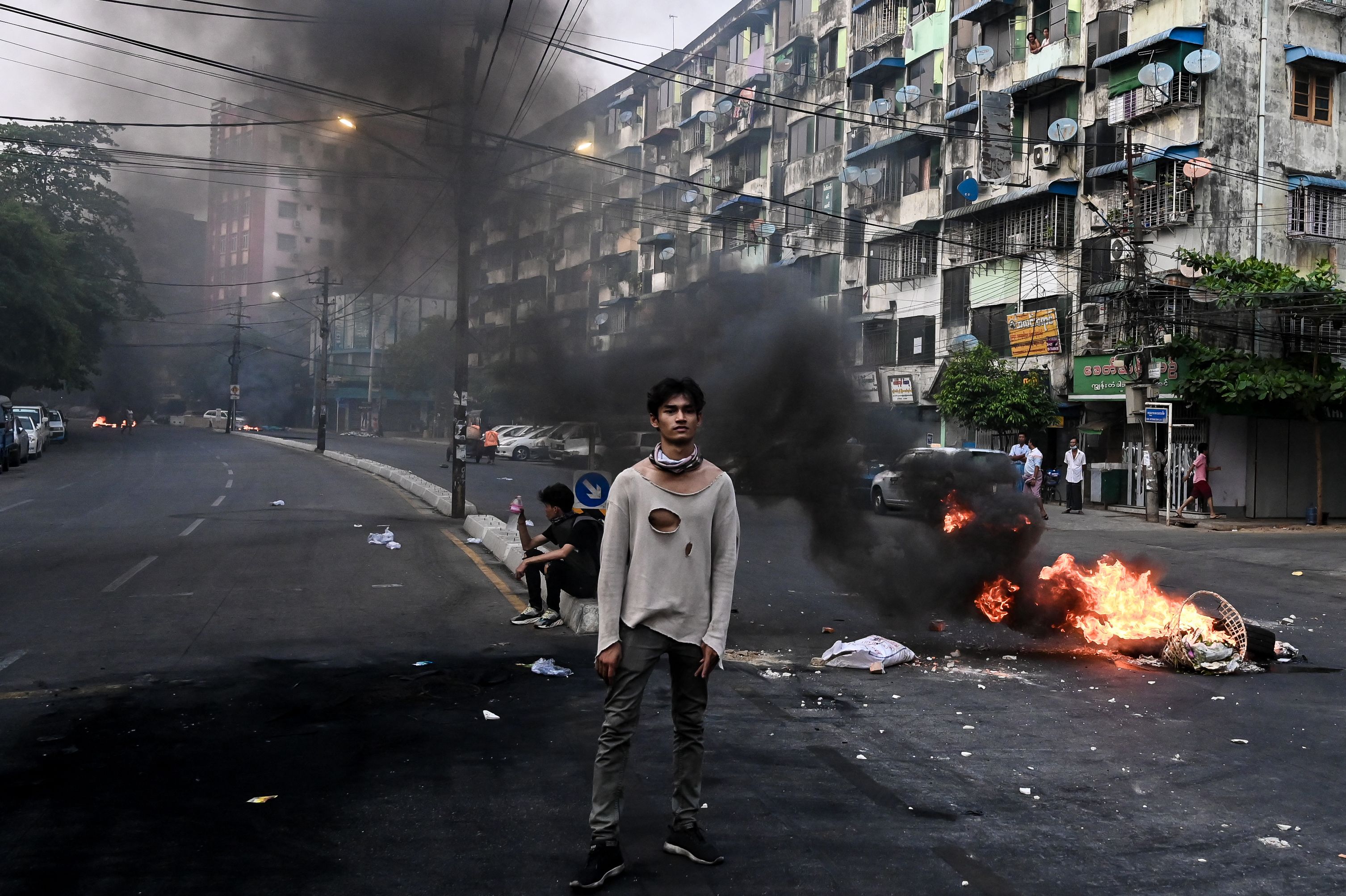 Seorang demonstran berdiri di dekat barikade yang terbakar di Yangon, Myanmar.