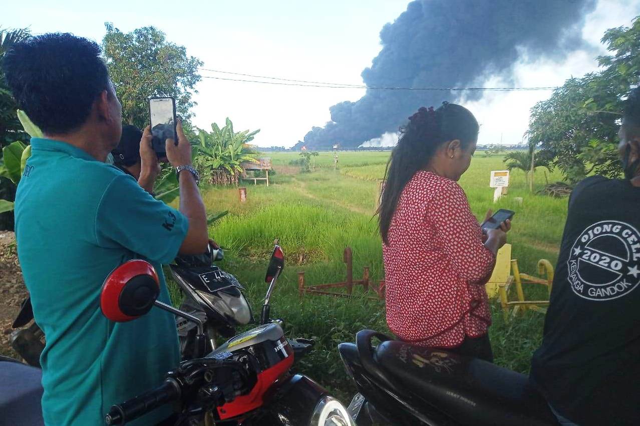  Sejumlah warga terlihat menonton asap hitam yang mengebul dari tangki di kilang Pertamina RU VI Balongan, Indramayu, Senin (29/3).