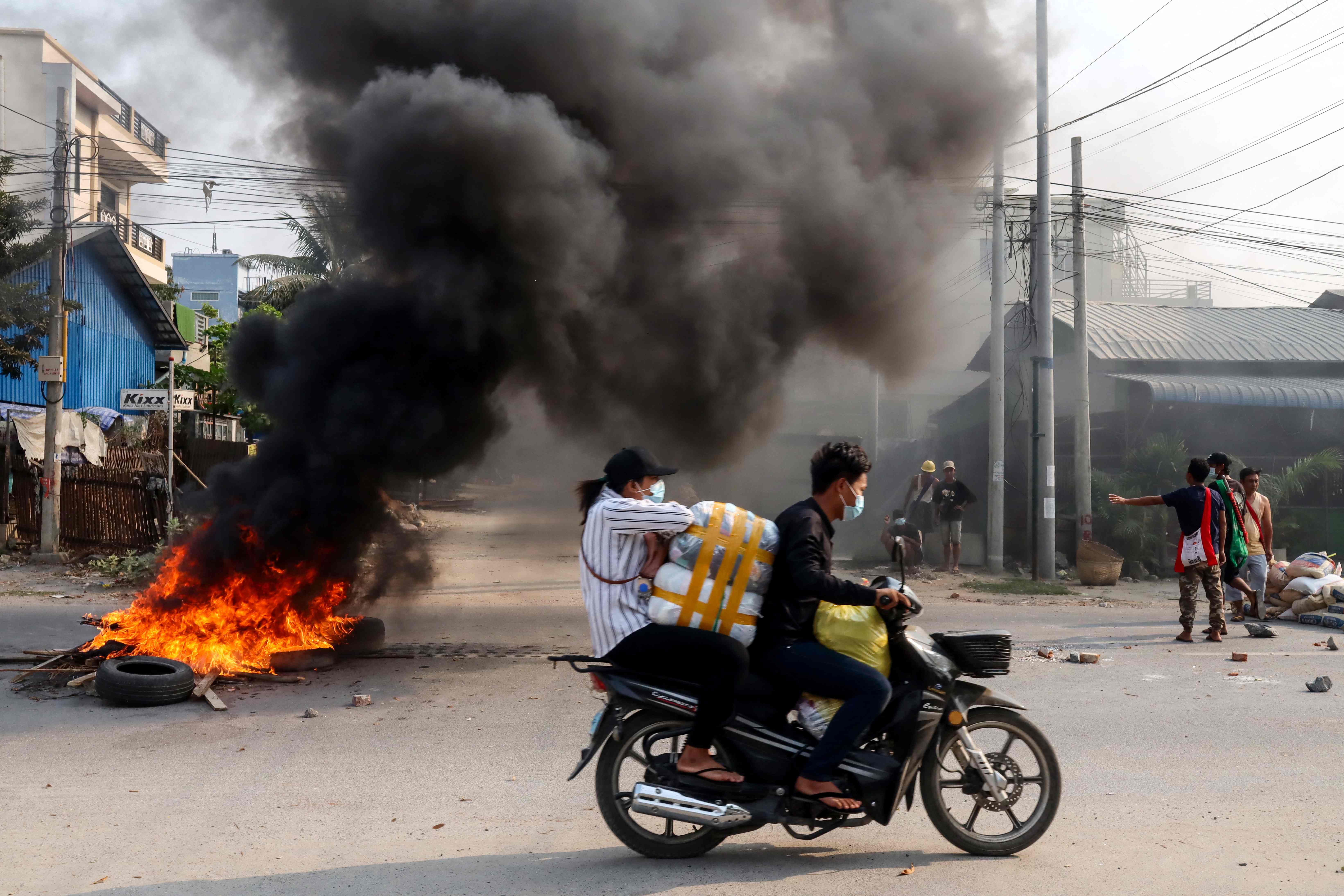 Warga melintas di dekat ban yang dibakar dalam aksi demonstrasi di Mandalay, Myanmar.