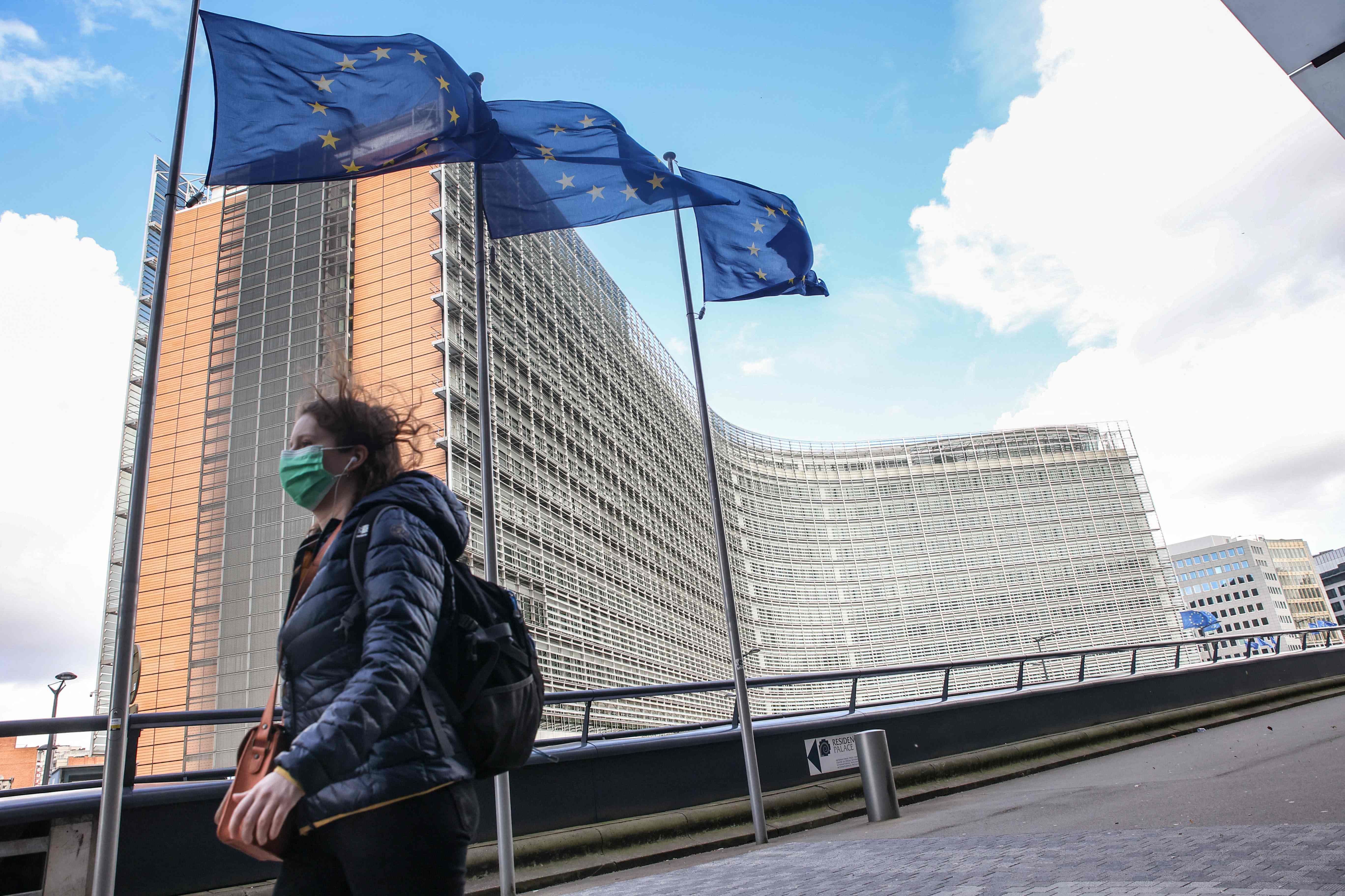 Pejalan kaki melintasi bendera yang terpasang di depan markas Uni Eropa di Brussels.