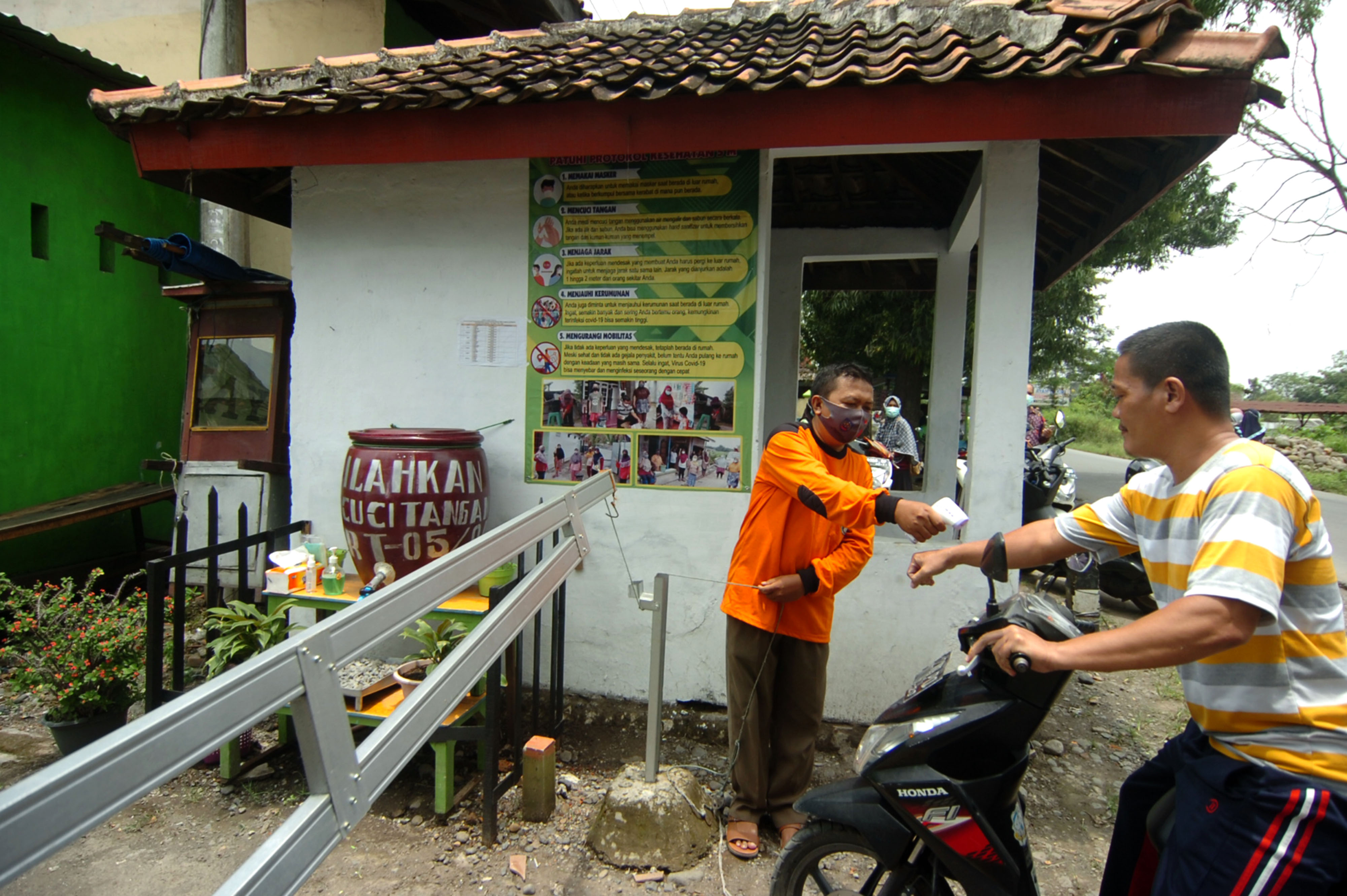 Petugas memeriksa suhu tubuh warga sebelum masuk ke kawasan Desa Mindaka, di Kabupaten Tegal, Jawa Tengah.