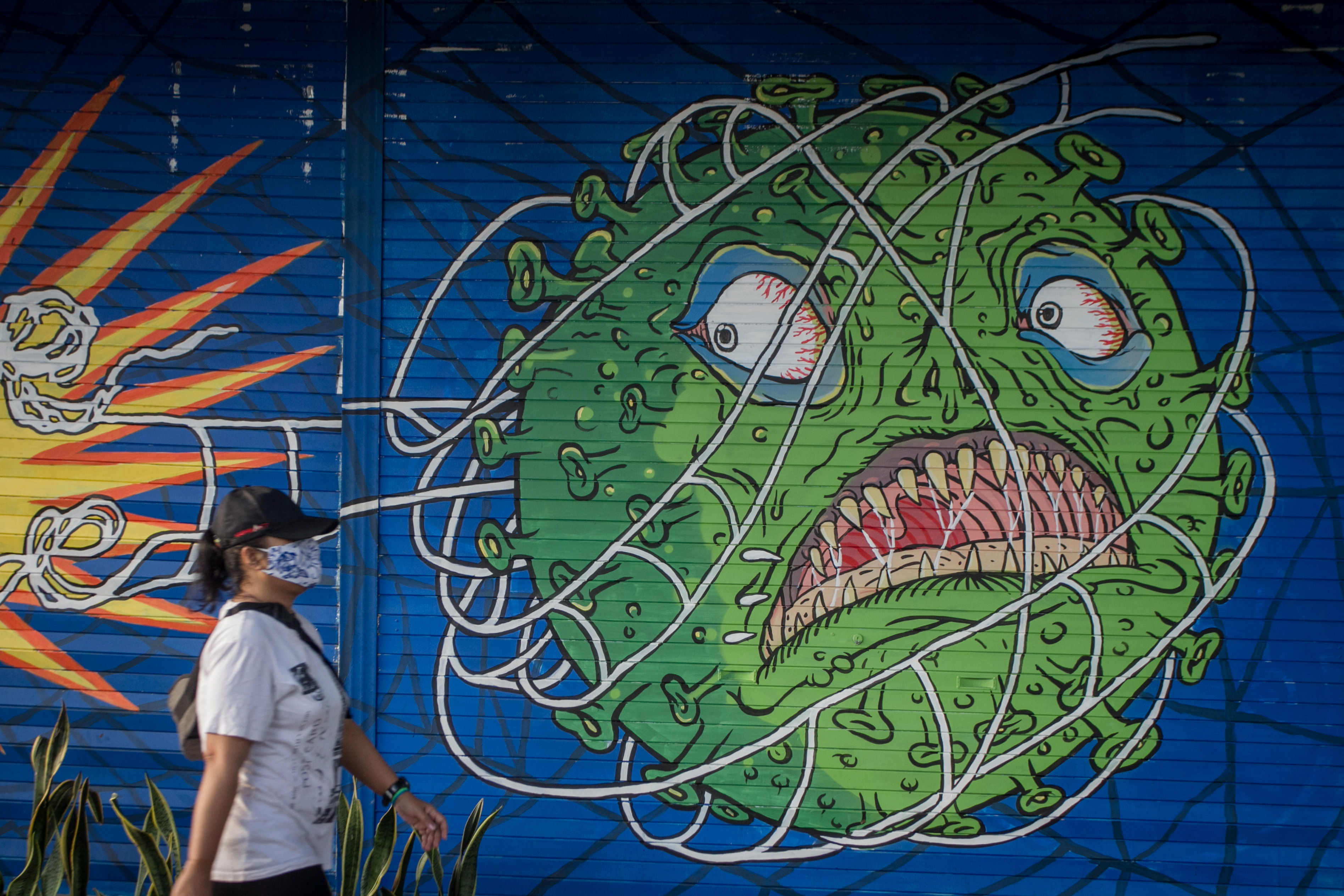  Warga melintas di depan mural bertema COVID-19 di Kemplayan, Solo, Jawa Tengah, Minggu (21/2).